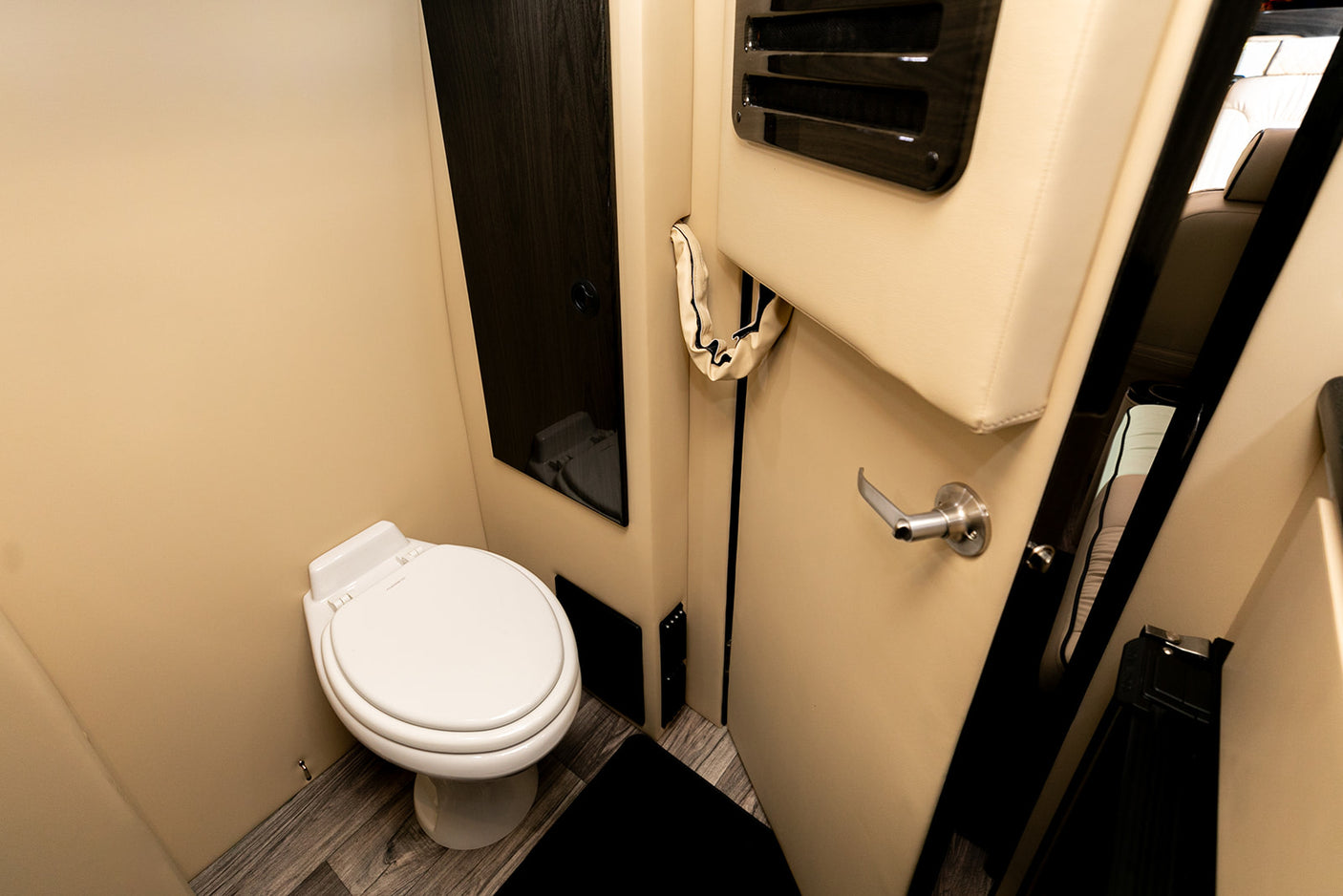 Compact RV rental bathroom: a white toilet against cream walls, dark wood accents, and laminate flooring for travel comfort.
