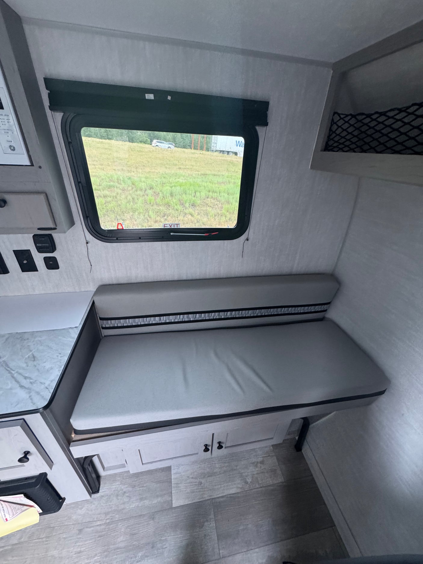 Cozy rv rental interior: a light grey bench dinette with striped backrest, window view of a field, and under-seat storage.