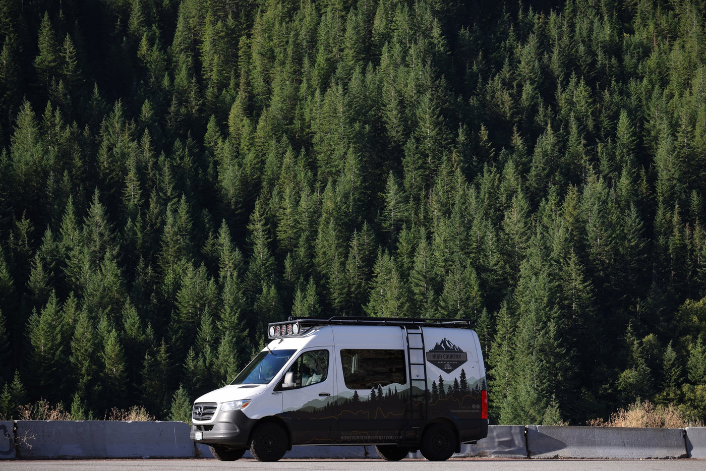 High Country Adventure RV rental van with mountain livery, parked beside a dense pine forest. — photo 10