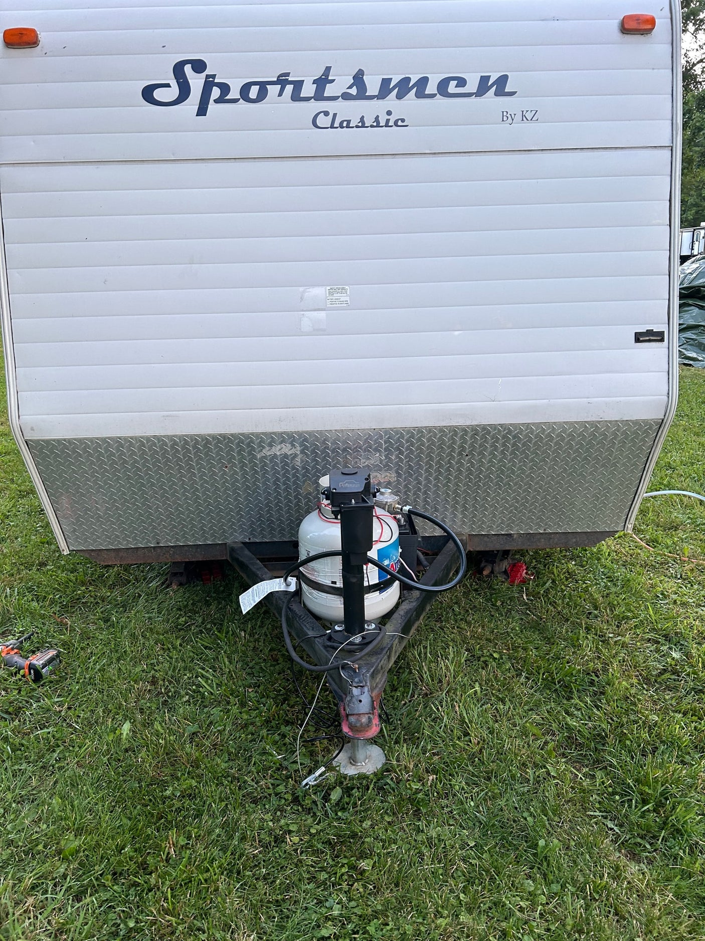 Front view of a white Sportsmen Classic RV rental (by KZ), showing its propane tank and hitch on green grass.