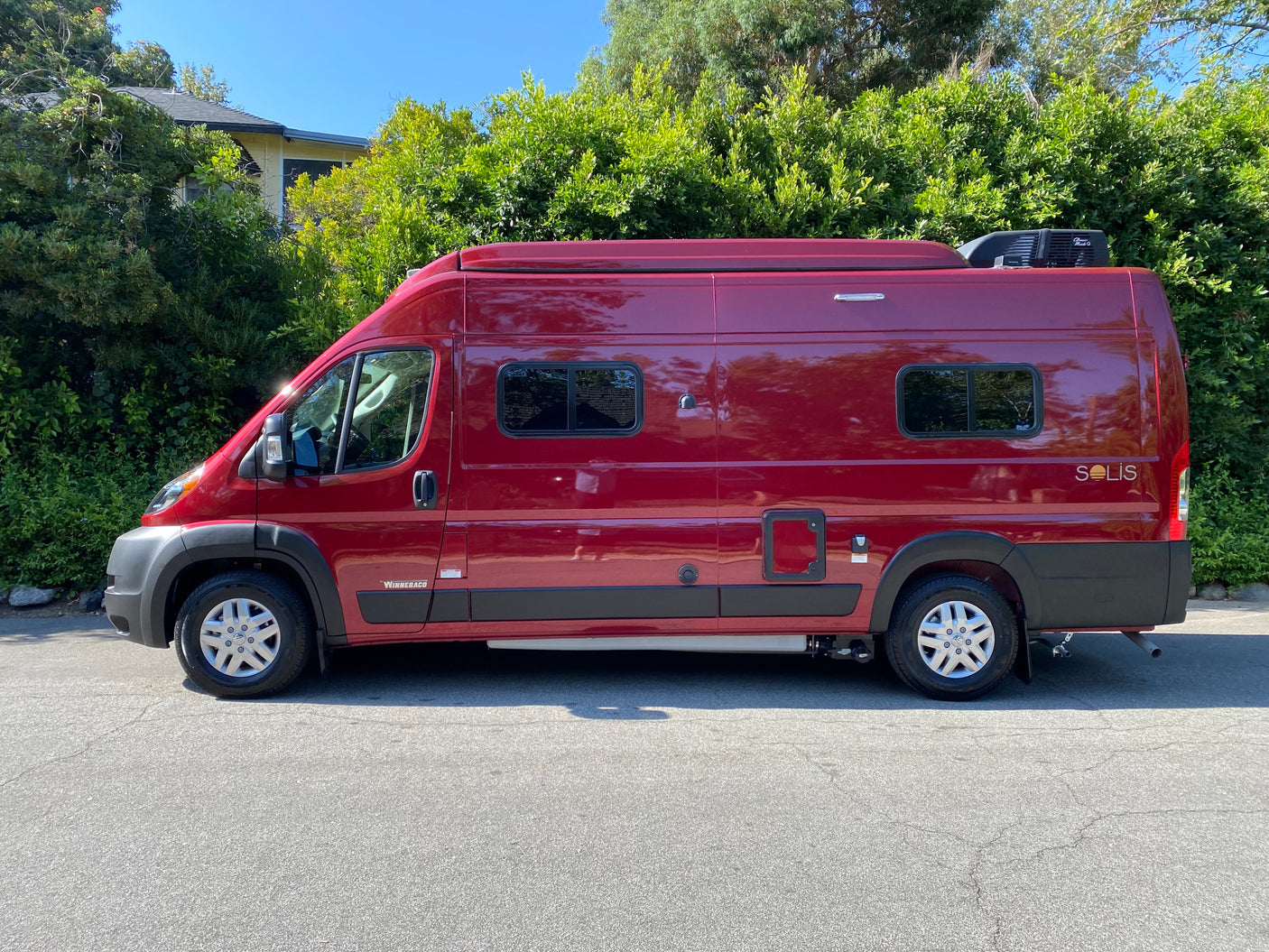 A vibrant red Winnebago Solis camper van, perfect for an RV rental adventure, parked on a sunny street.