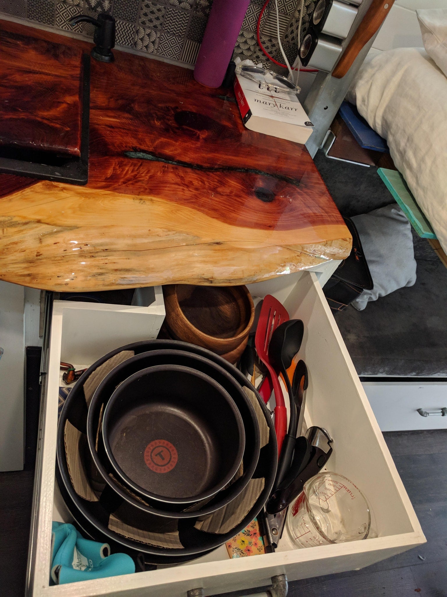 RV rental: Kitchen counter with live-edge wood, a sink, and a pull-out drawer full of organized pots & cooking tools.
