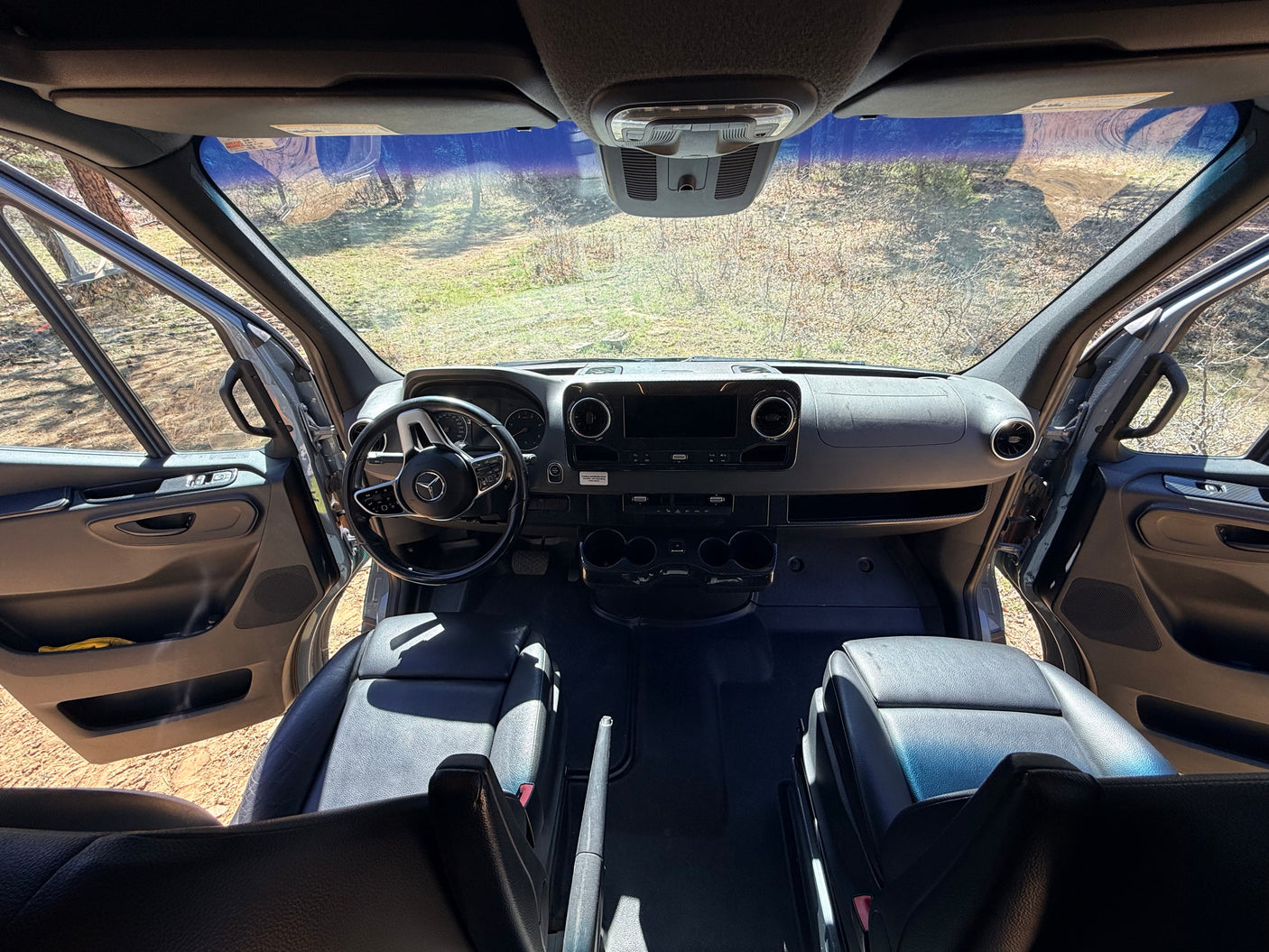 Spacious rv rental cabin view from rear, featuring dashboard, steering wheel, front seats, and open doors to nature.
