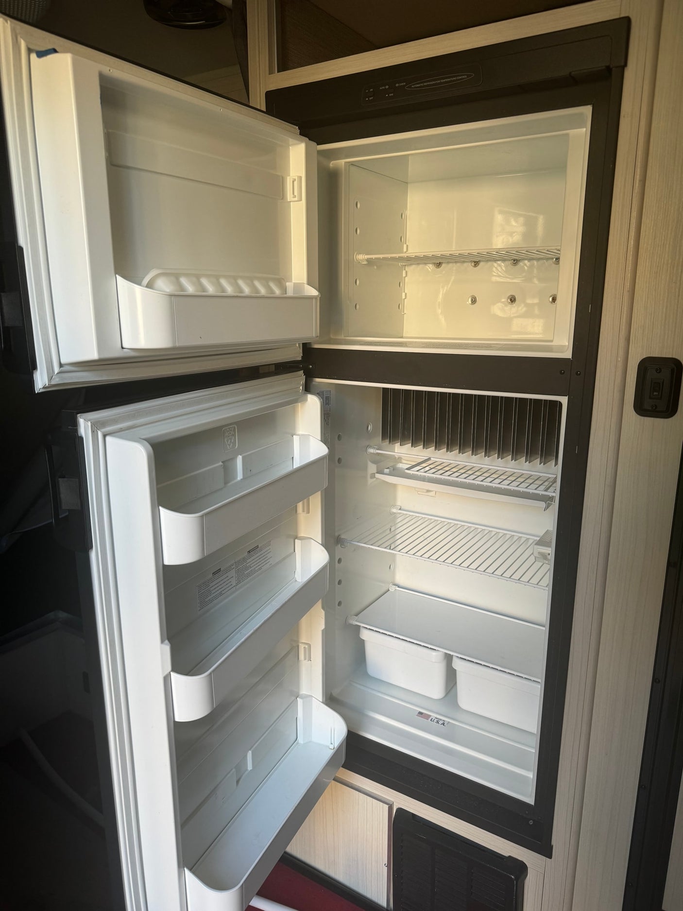 Inside a clean, empty RV refrigerator, ready for your rv rental. Both doors are open, revealing shelves and door bins.
