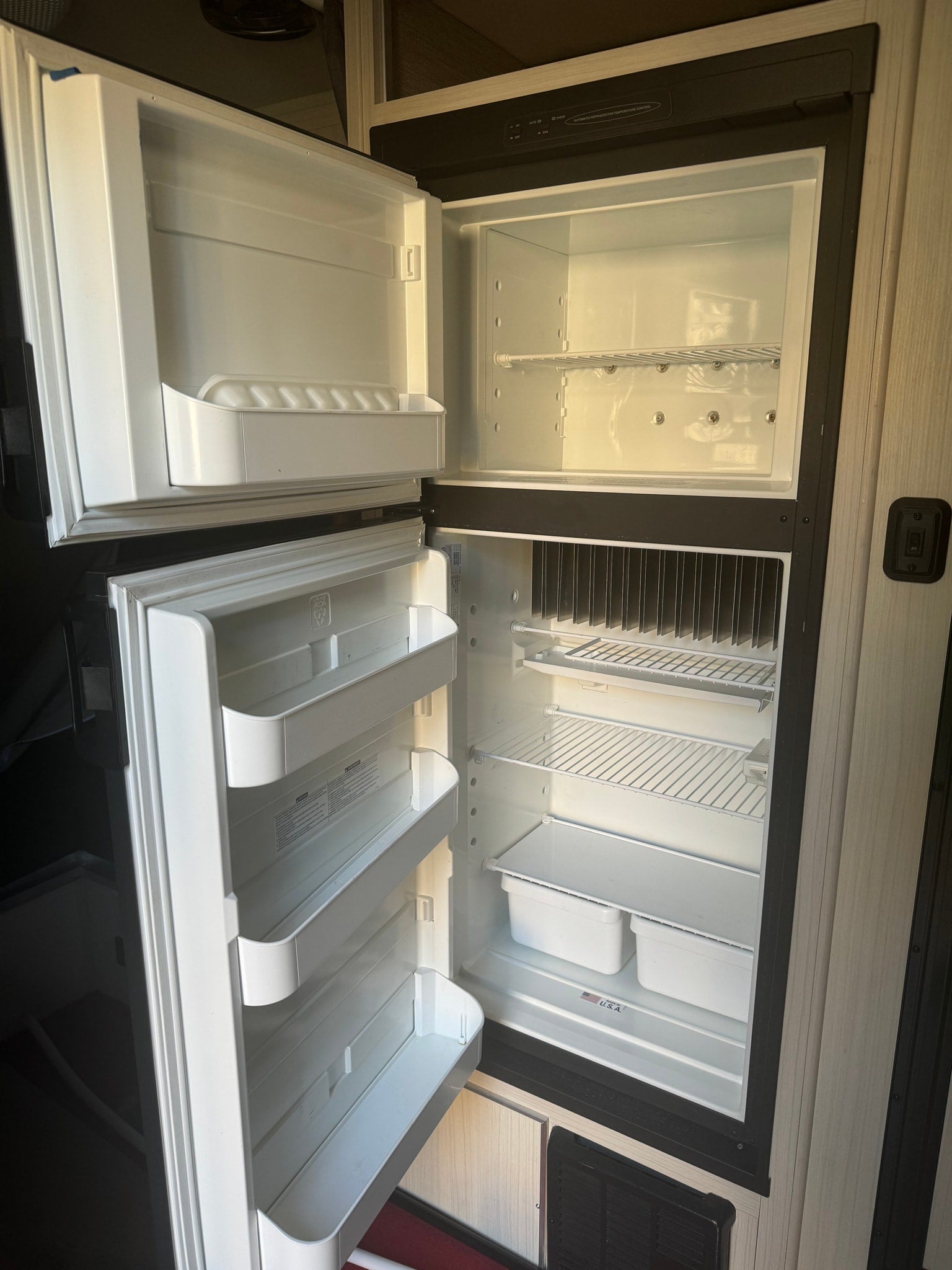 Inside a clean, empty RV refrigerator, ready for your rv rental. Both doors are open, revealing shelves and door bins.