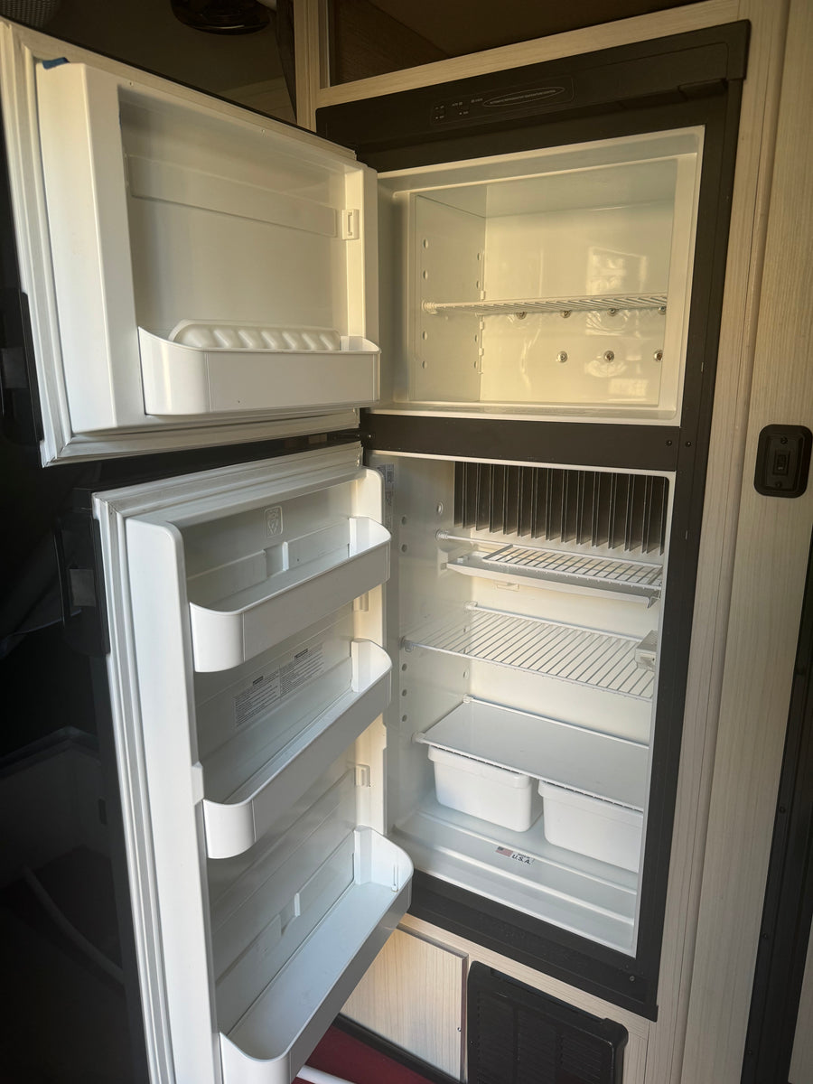 Inside a clean, empty RV refrigerator, ready for your rv rental. Both doors are open, revealing shelves and door bins.