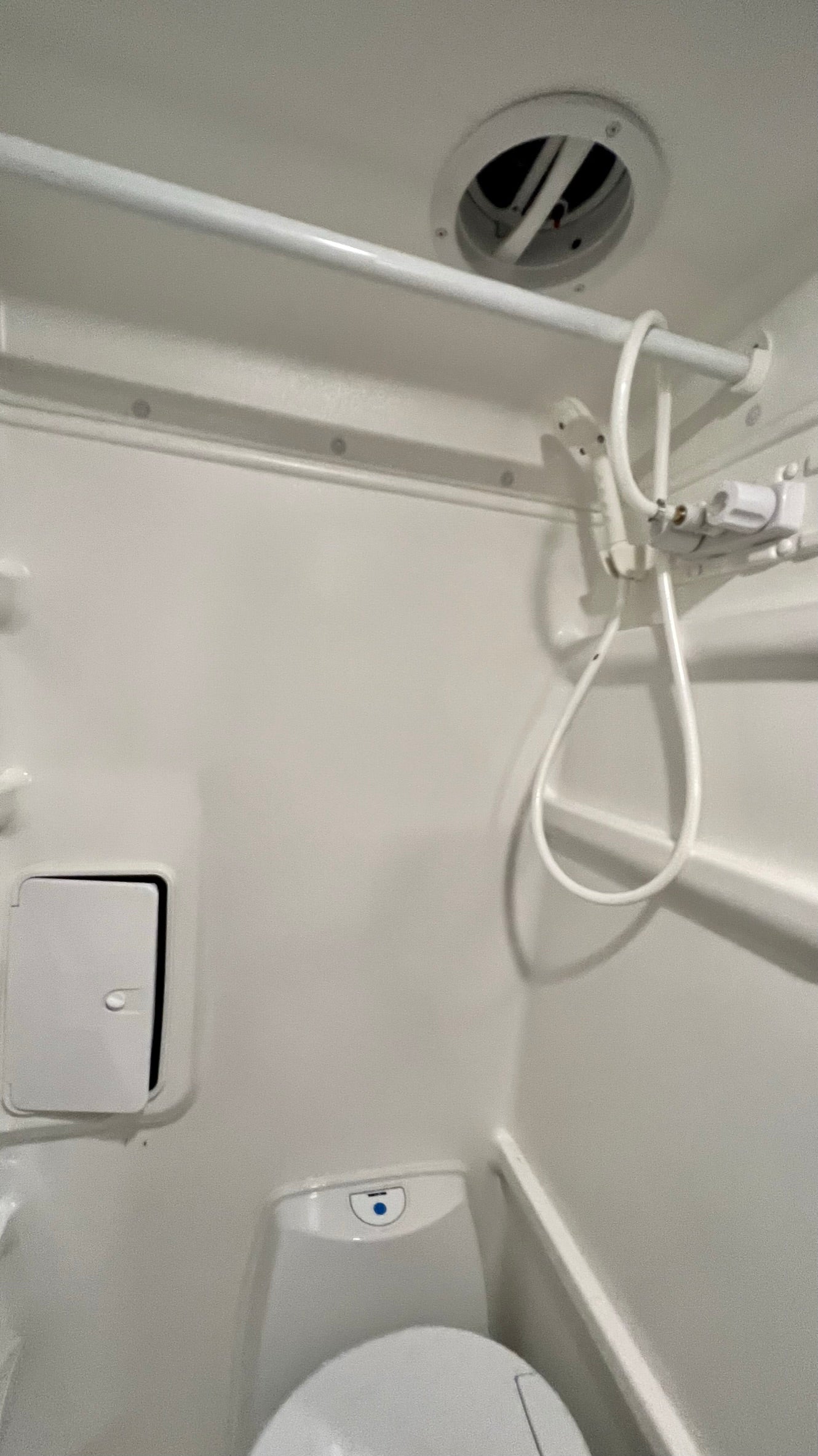 Inside this compact RV rental bathroom: an all-white design with a toilet, handheld shower, and ceiling vent.