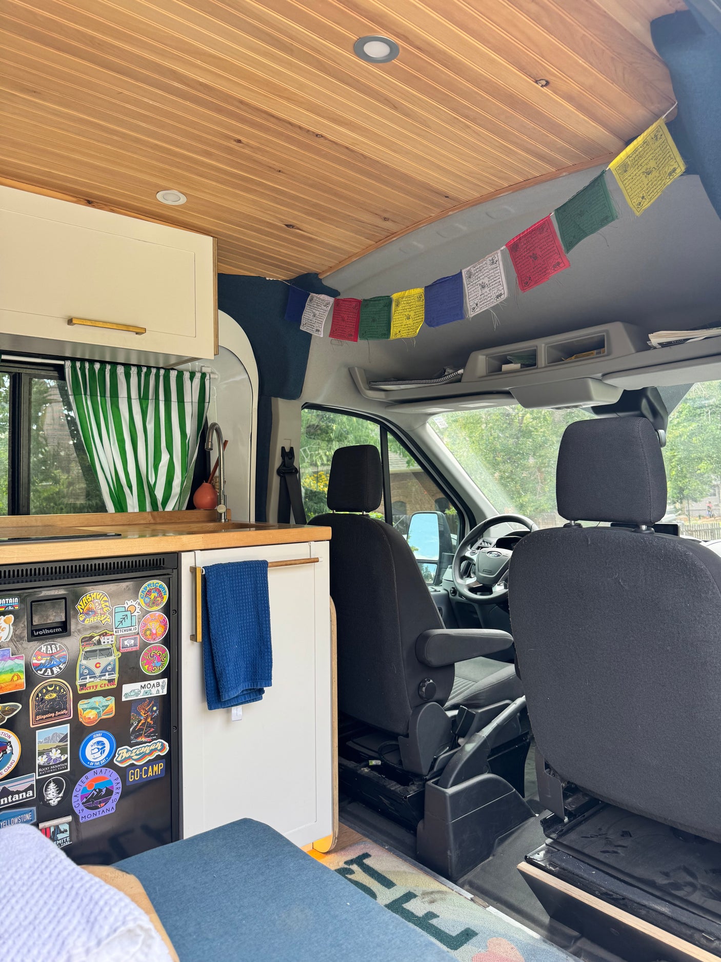 Cozy RV rental interior: custom camper van with wooden ceiling, kitchen, and a fridge adorned with travel stickers.