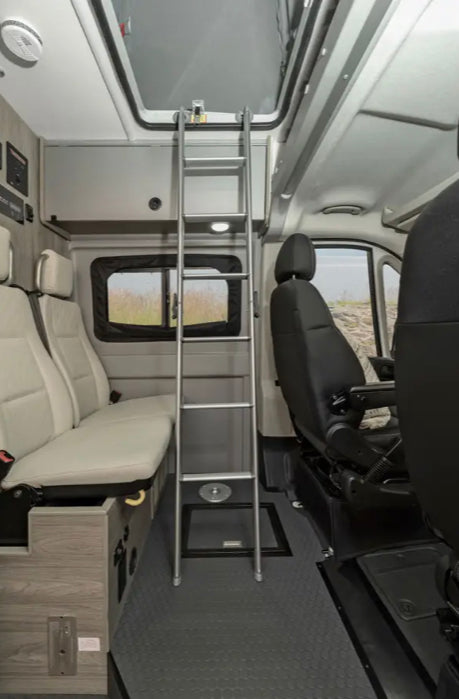 Spacious RV rental interior: a ladder leads to an upper bunk. Features comfortable seating, windows, and overhead storage.