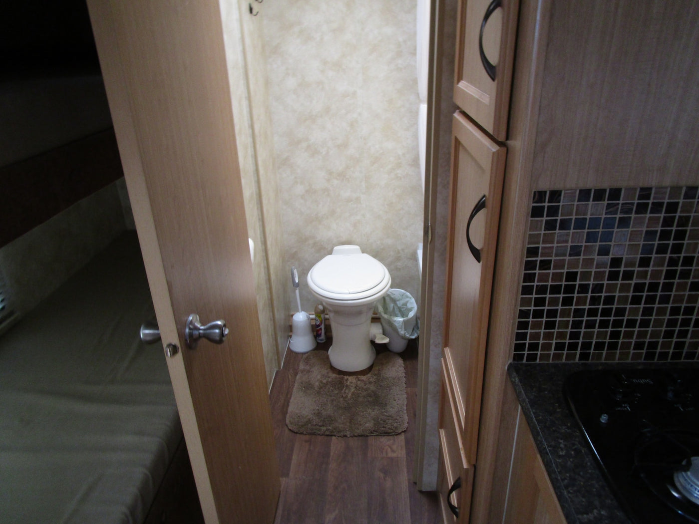 Inside an RV rental: a compact bathroom with toilet, comfortable bed area, and efficient kitchen with stovetop & cabinets. — photo 8