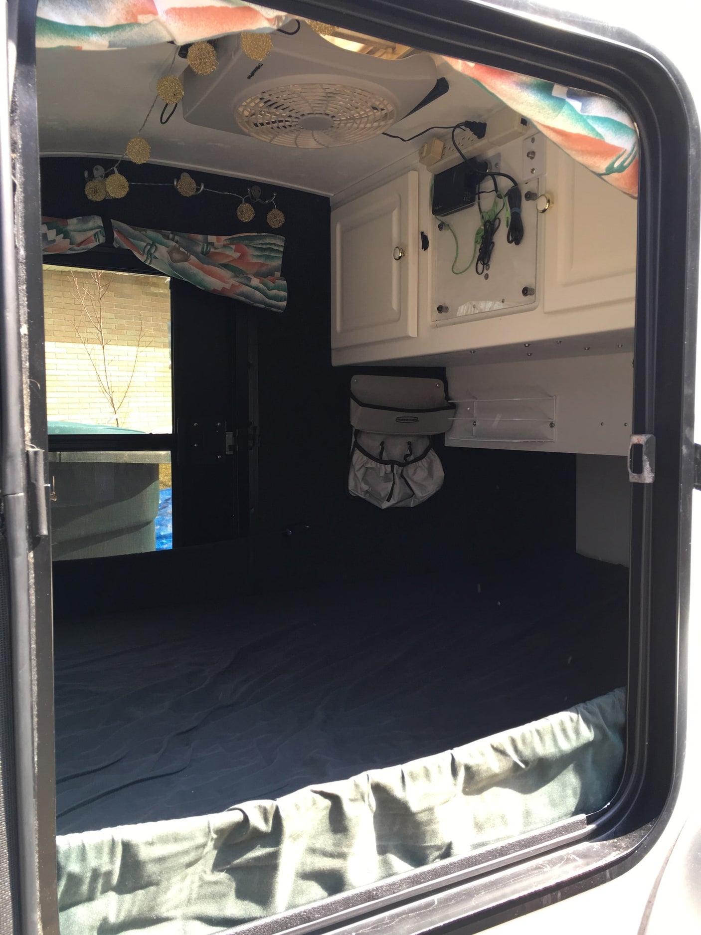 Inside a cozy RV rental: bed, overhead storage, fan, and string lights, ready for adventure.