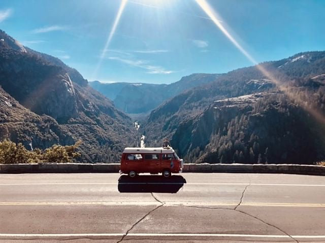 Stunning mountain valley view with a red camper van on the road. Plan your next scenic RV rental adventure through breathtaking landscapes.