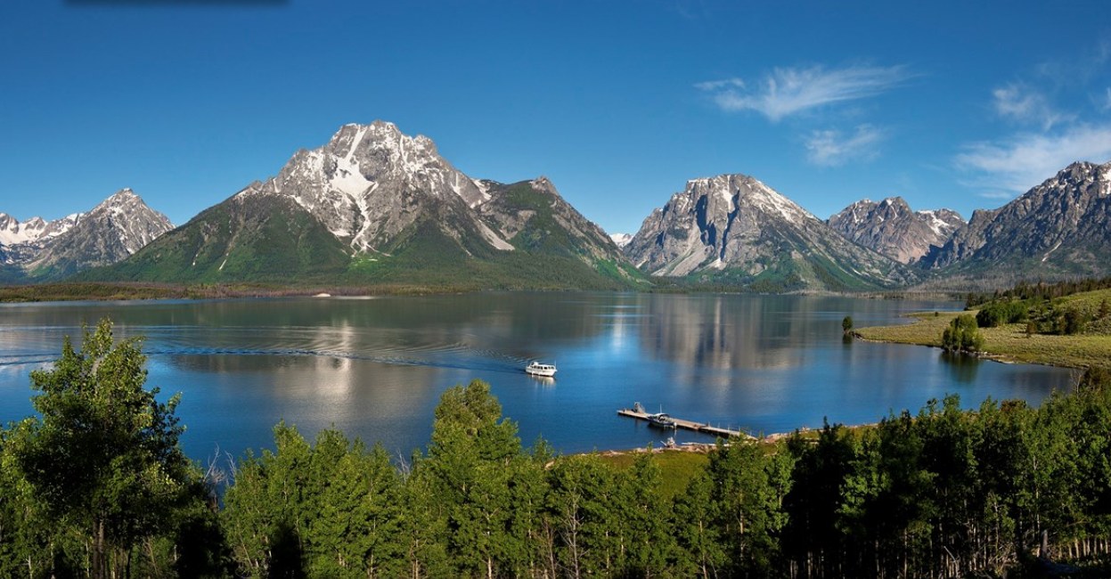Stunning mountain-lake vista with a boat and dock. Your RV rental adventure awaits in this pristine national park.