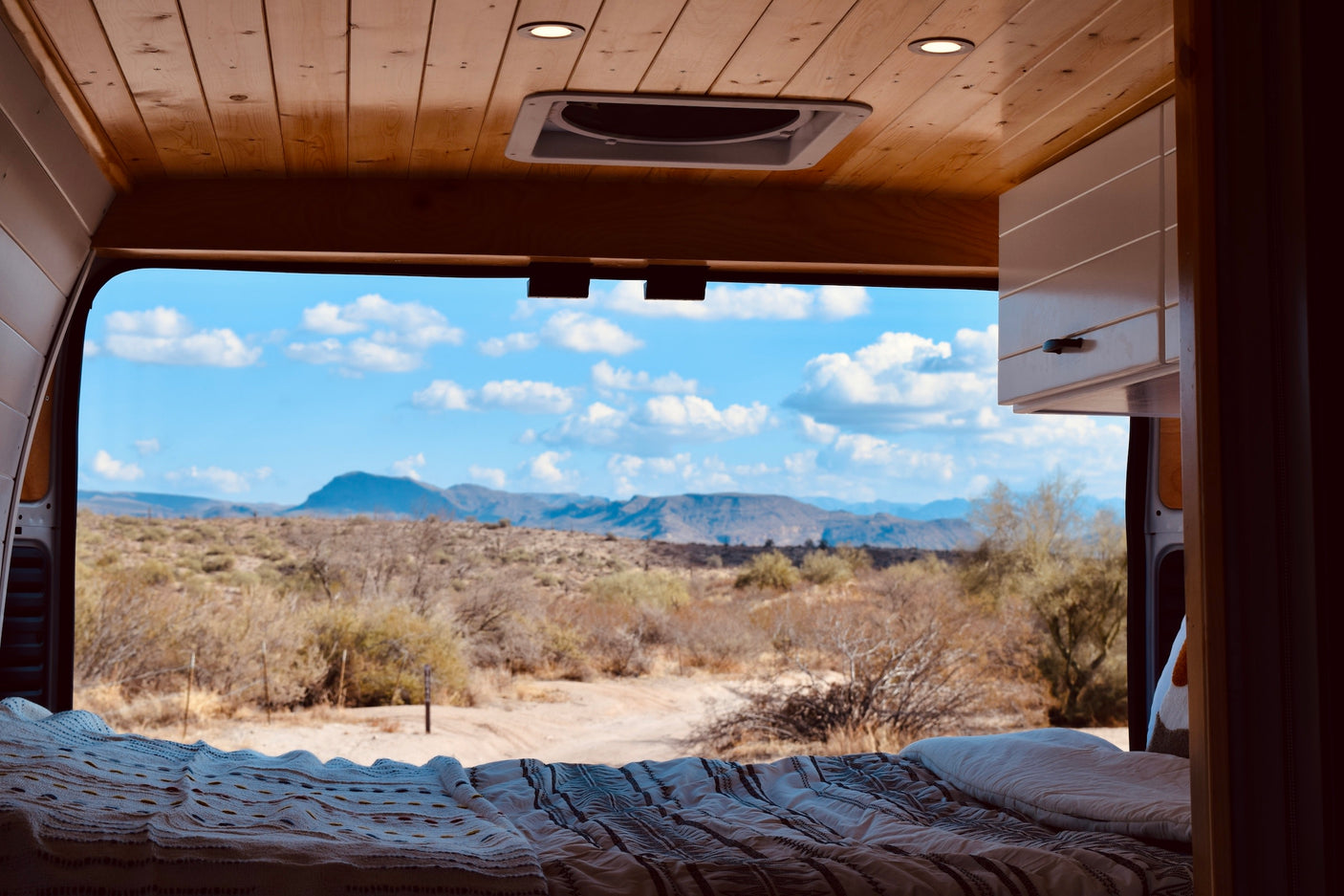 RV rental interior looking out at a scenic desert mountain view. Features wooden ceiling, fan, bed & cabinets. #vanlife #adventure