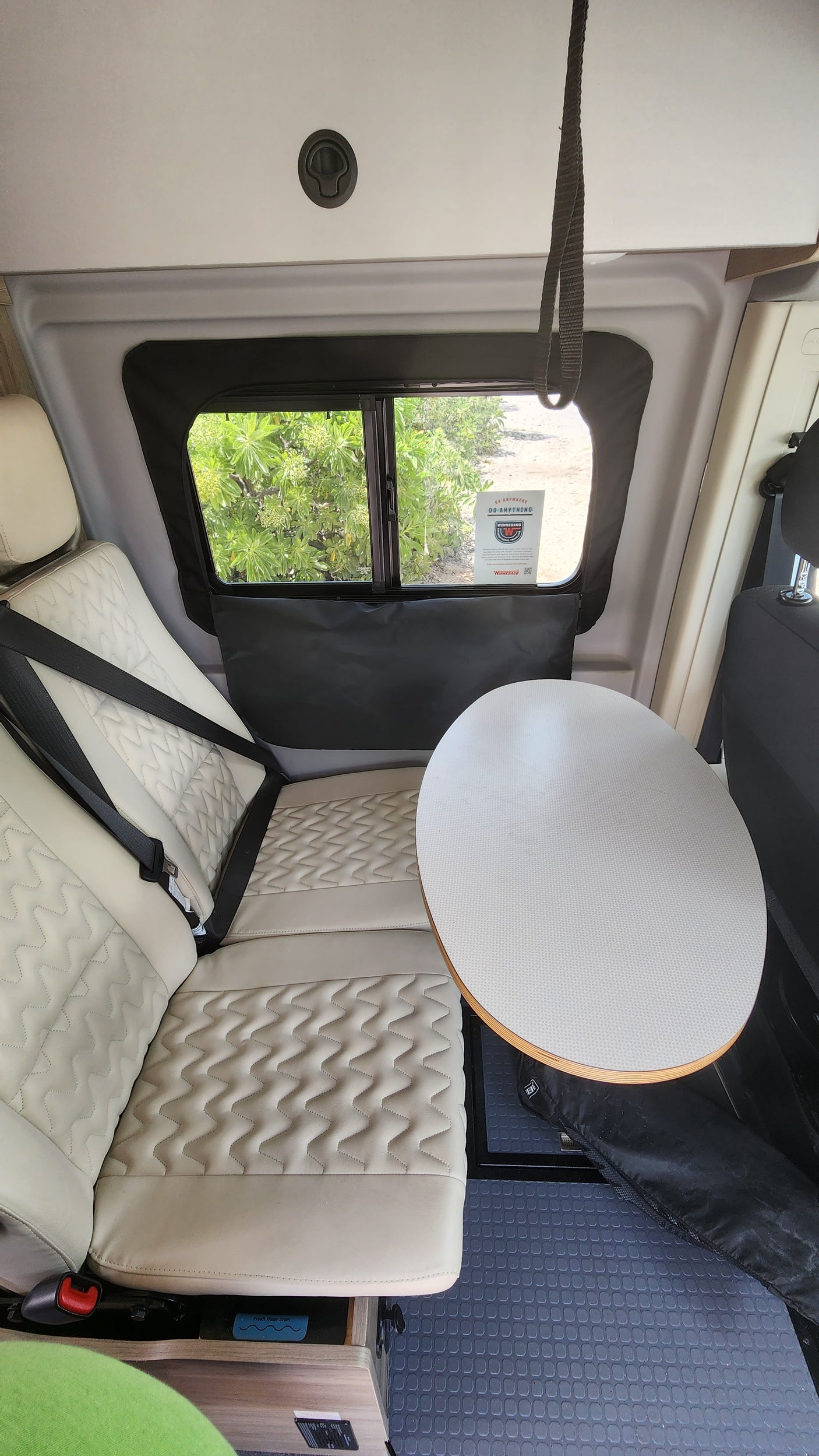 RV rental interior with comfy seating, a suspended table, and a window view of lush greenery, ideal for travel.