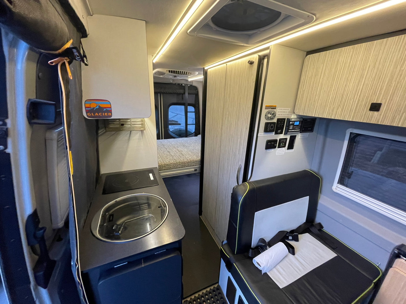 Compact rv rental camper van interior featuring a kitchen, comfortable seating, and a cozy bed area under bright LED lights.