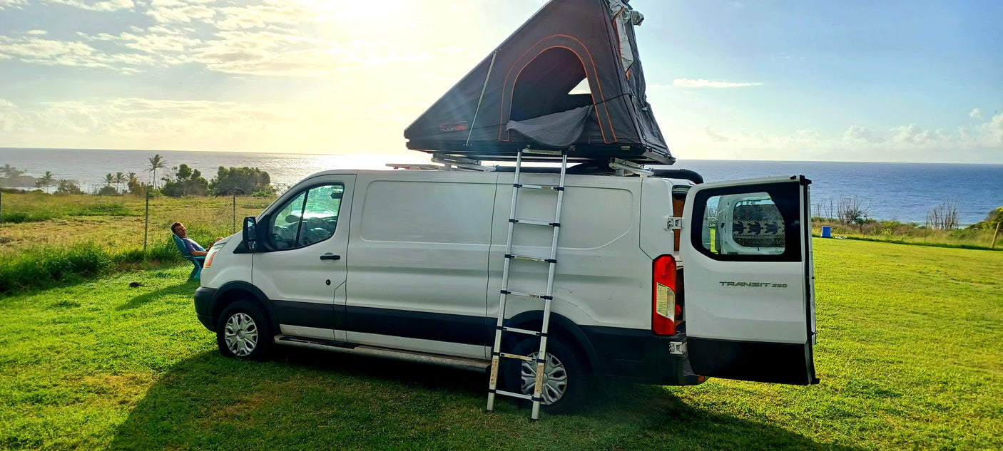 This RV rental van, a white Ford Transit 250 with a rooftop tent and ladder, offers stunning ocean views for camping & van life.