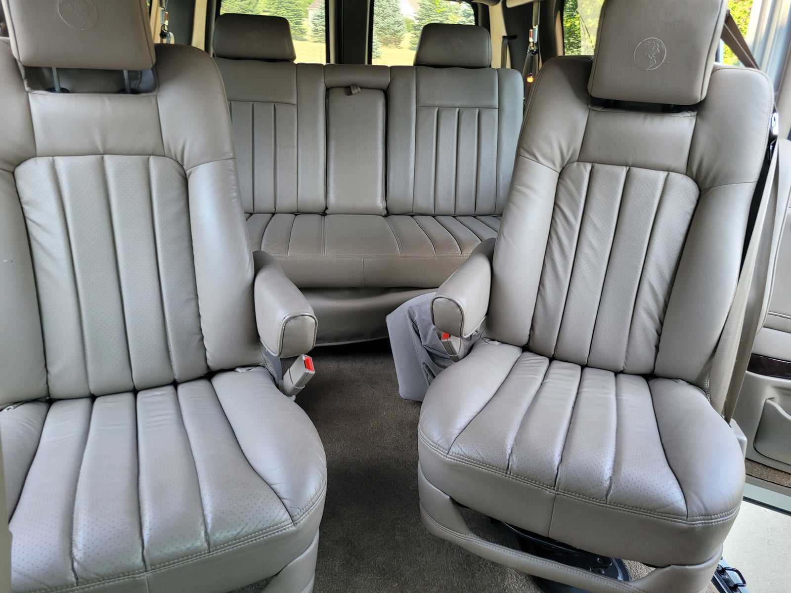 two captain's chairs & rear bench for comfort.|White van rv rental parked by a tranquil lake with forested mountains. Perfect for scenic road trips.|Comfortable Chevrolet RV interior