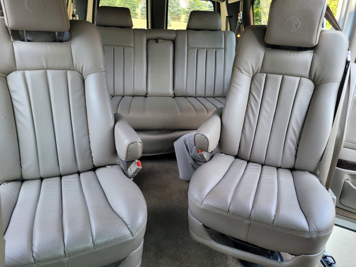 two captain's chairs & rear bench for comfort.|White van rv rental parked by a tranquil lake with forested mountains. Perfect for scenic road trips.|Comfortable Chevrolet RV interior