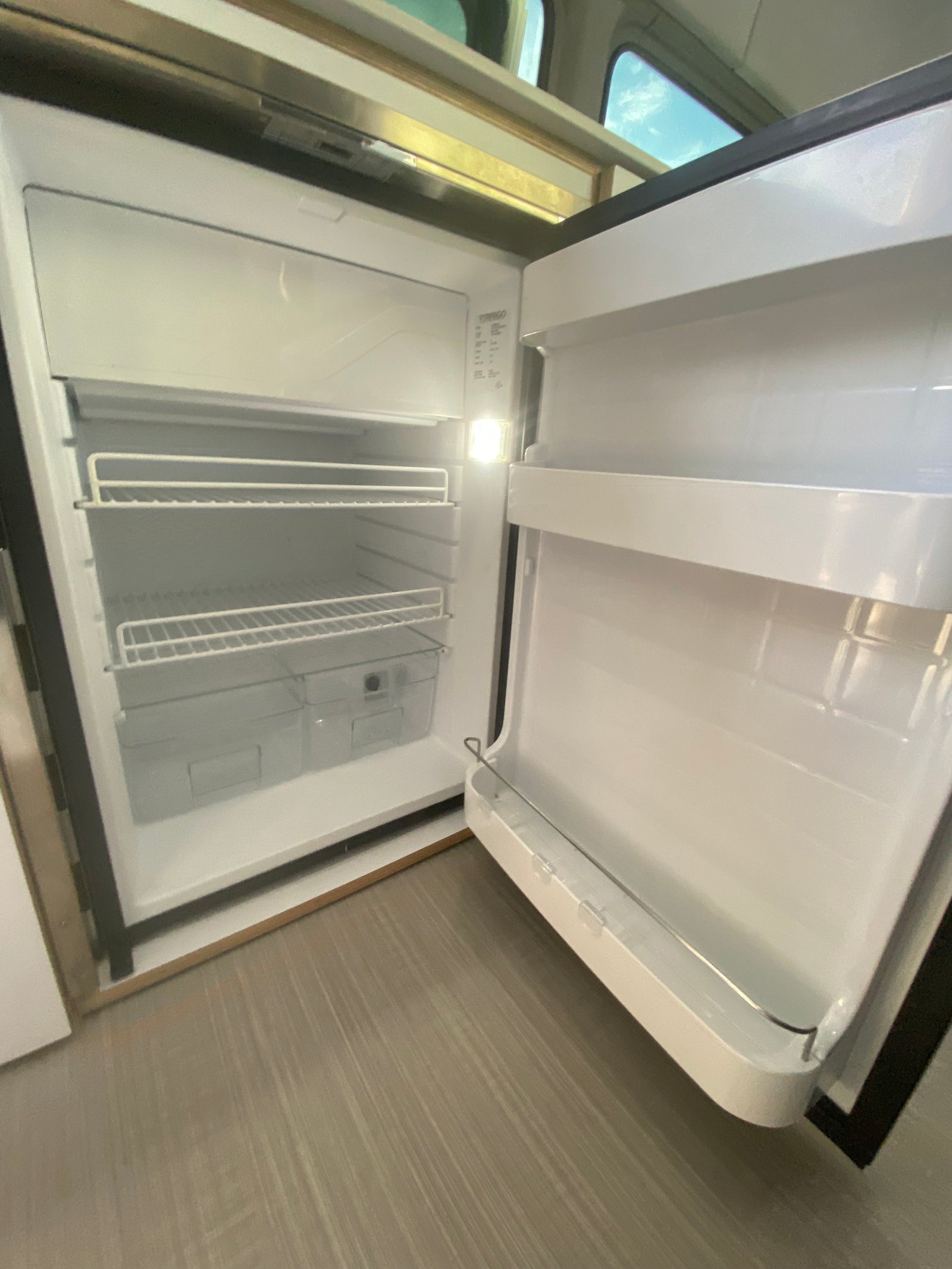 An open, clean RV rental refrigerator with shelves and crisper, ready for your travel provisions.