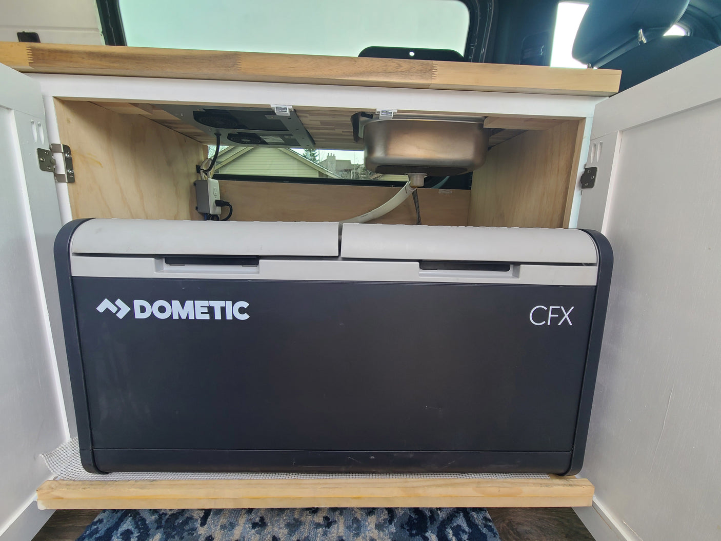 RV rental van's compact kitchen setup: Dometic CFX fridge, sink, and cooktop, ideal for road trip cooking & storage.