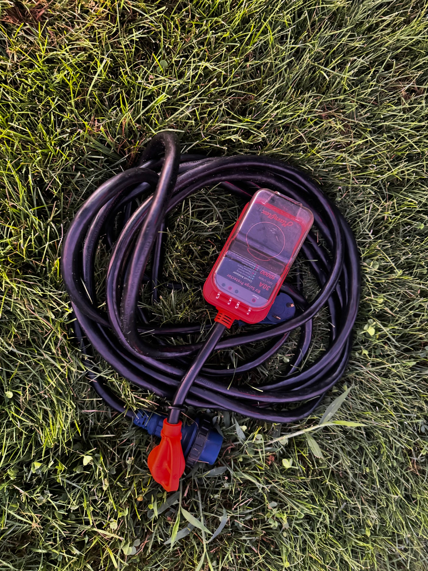 Essential for **rv rental** trips: A 30A RV power cord coiled on grass with a MarsFlex surge protector for safe hookups.