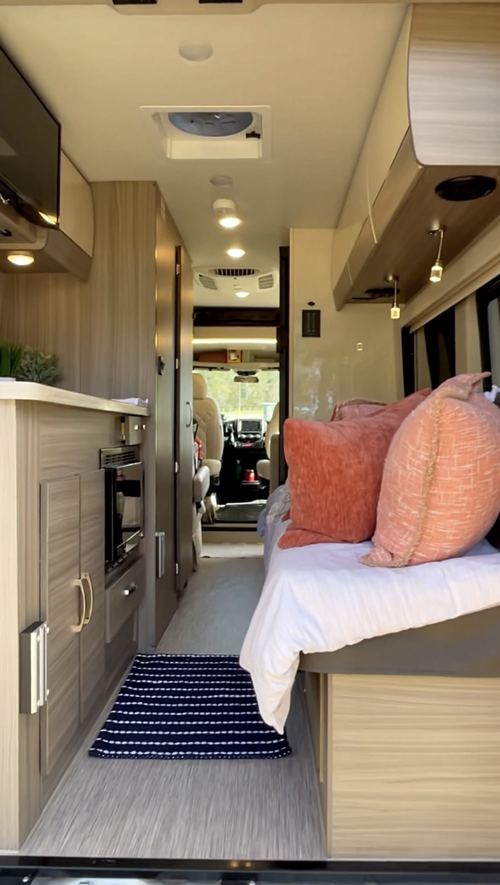Cozy RV rental interior with light wood cabinetry, a comfortable bed, compact kitchen area, and view to the front cabin.