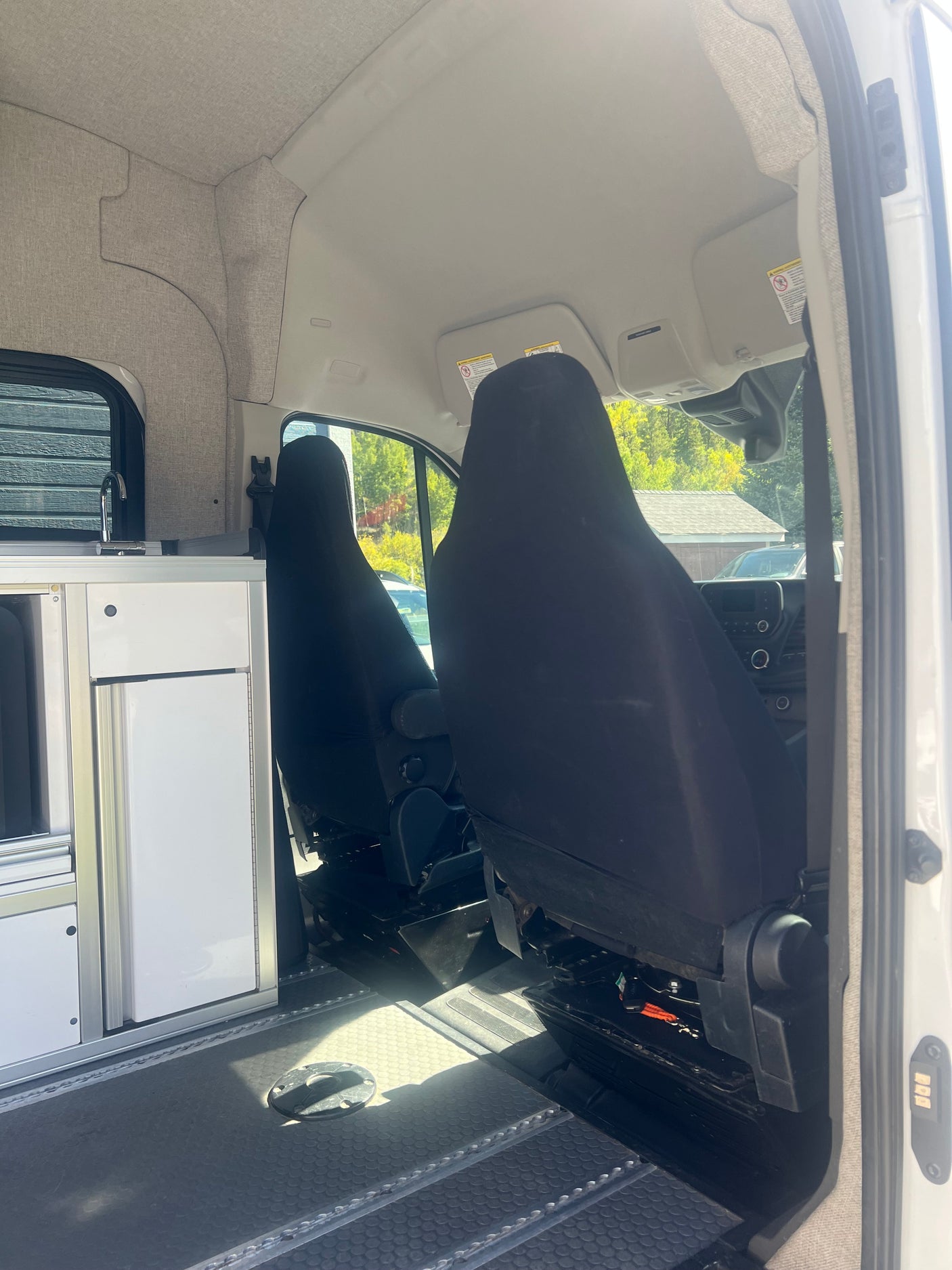 Bright rv rental camper van interior. Front seats, modular kitchen with sink, fabric-lined walls, and textured floor with tracks.