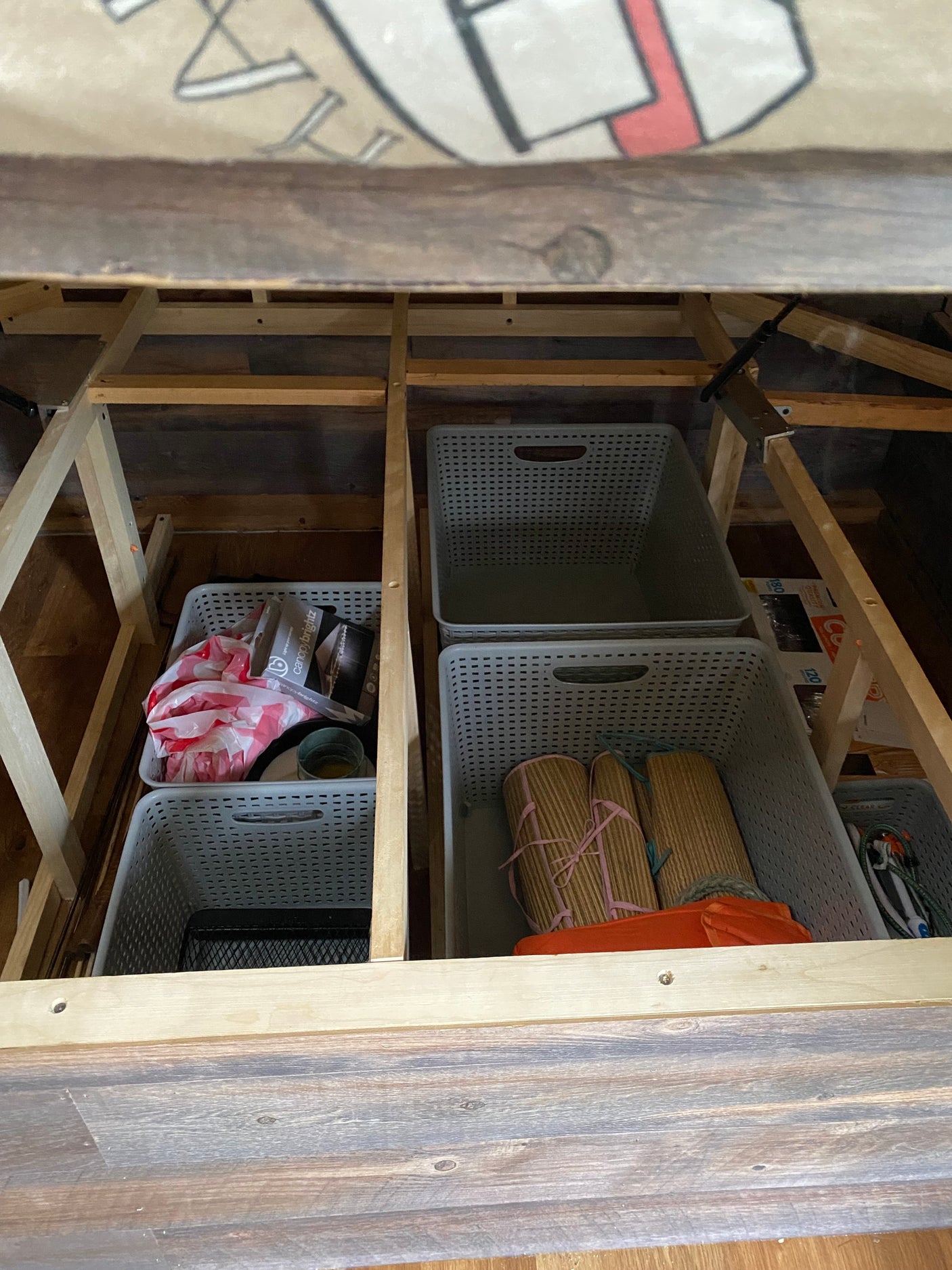 Efficient RV rental storage: neatly organized under-bed space with multiple grey baskets holding various items like rolled mats & bags.