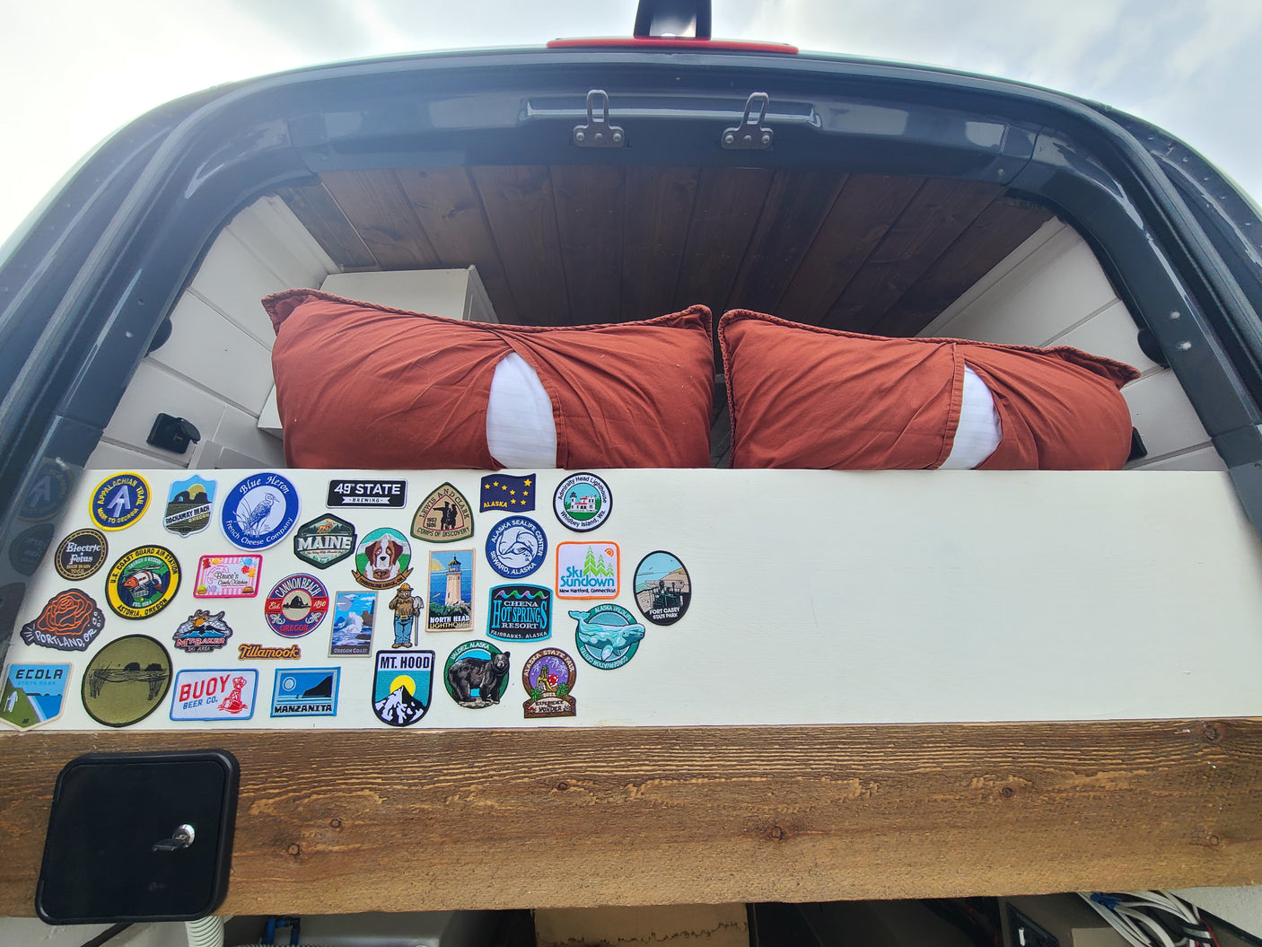 Cozy RV rental bed with pillows & a wall of travel patches showcasing US state parks & landmarks visited.