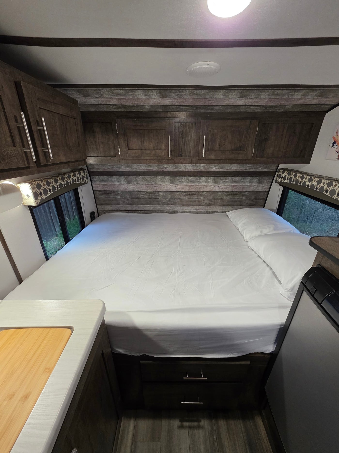 Cozy RV rental bedroom with a neatly made bed, wood cabinets, and windows offering nature views. — photo 6