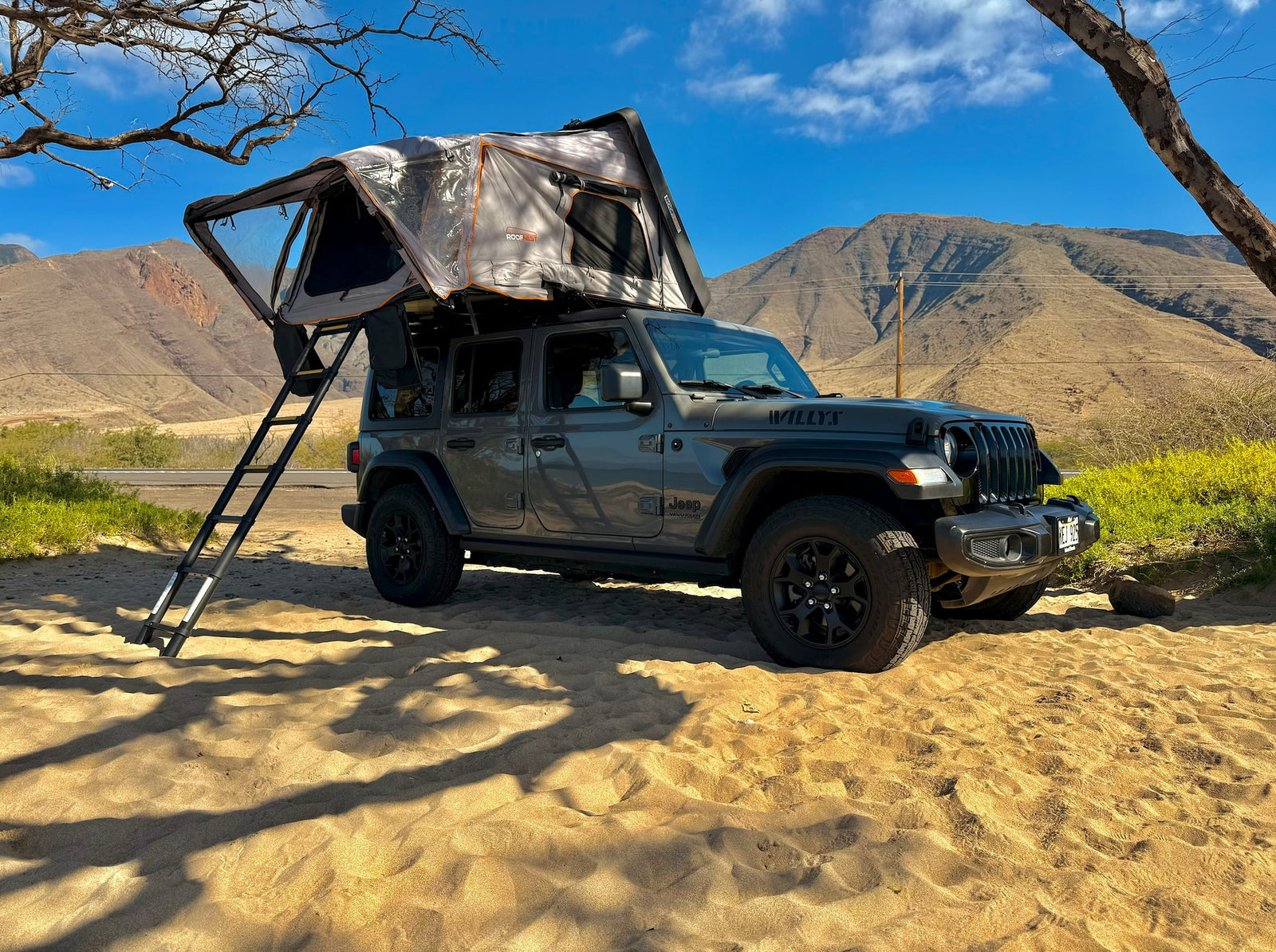 RV rental: Grey Jeep Wrangler with rooftop tent & ladder, on sand with mountains. Perfect for adventure!