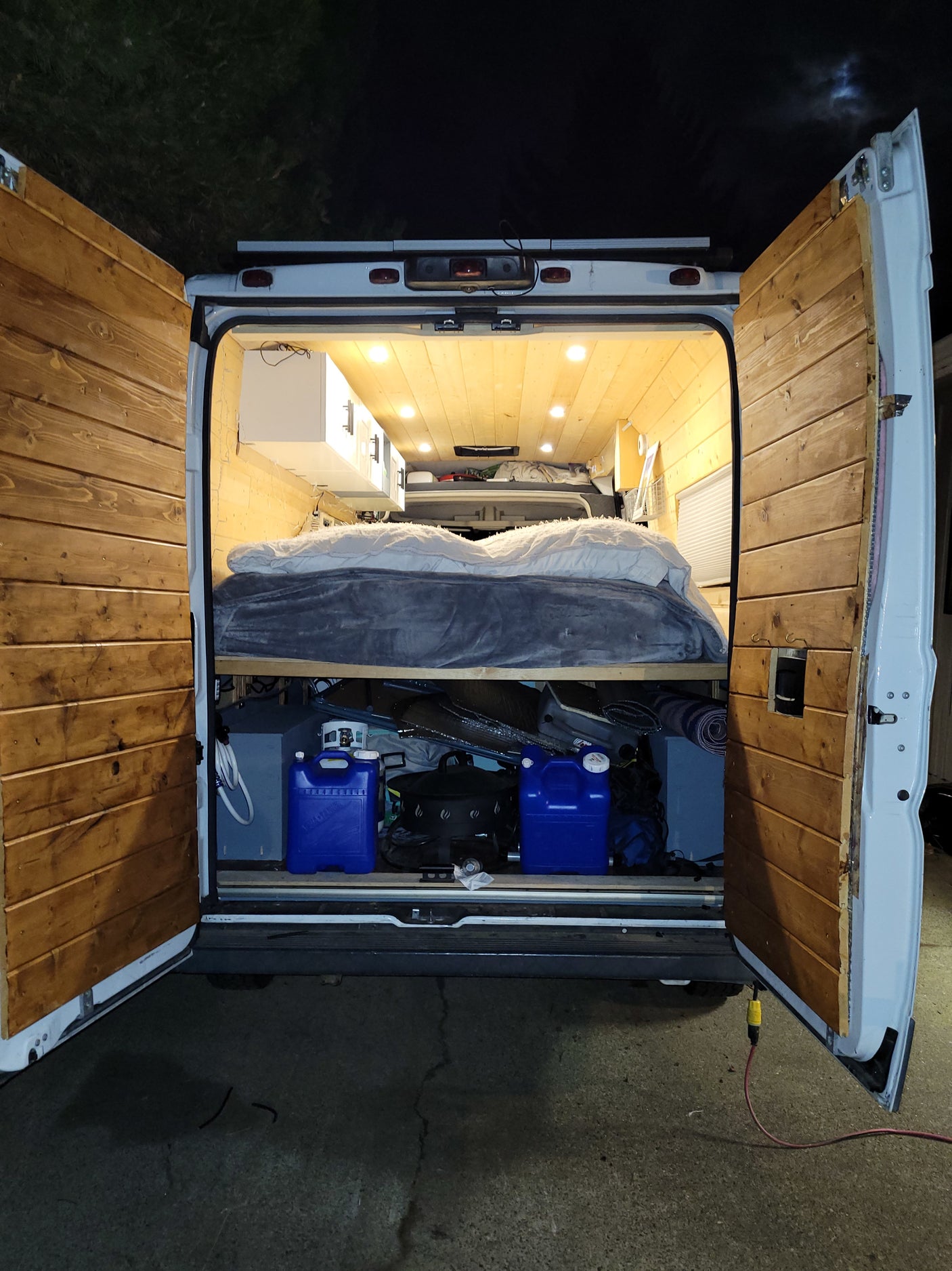 Inside this **rv rental** camper van: a wood-paneled interior with a bed, under-bed storage, and bright lights. Perfect for off-grid travel.
