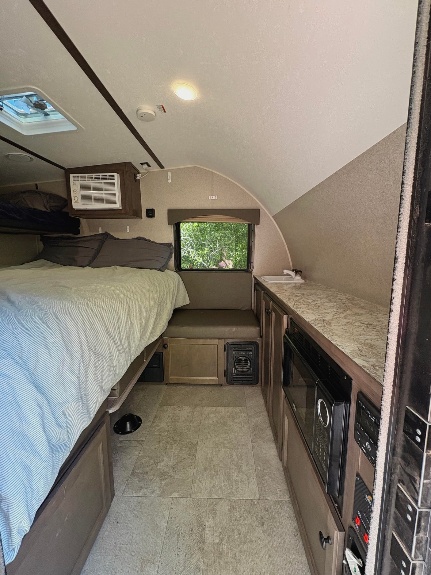 RV rental interior featuring a cozy bed, compact kitchenette, window view, and functional design elements throughout.