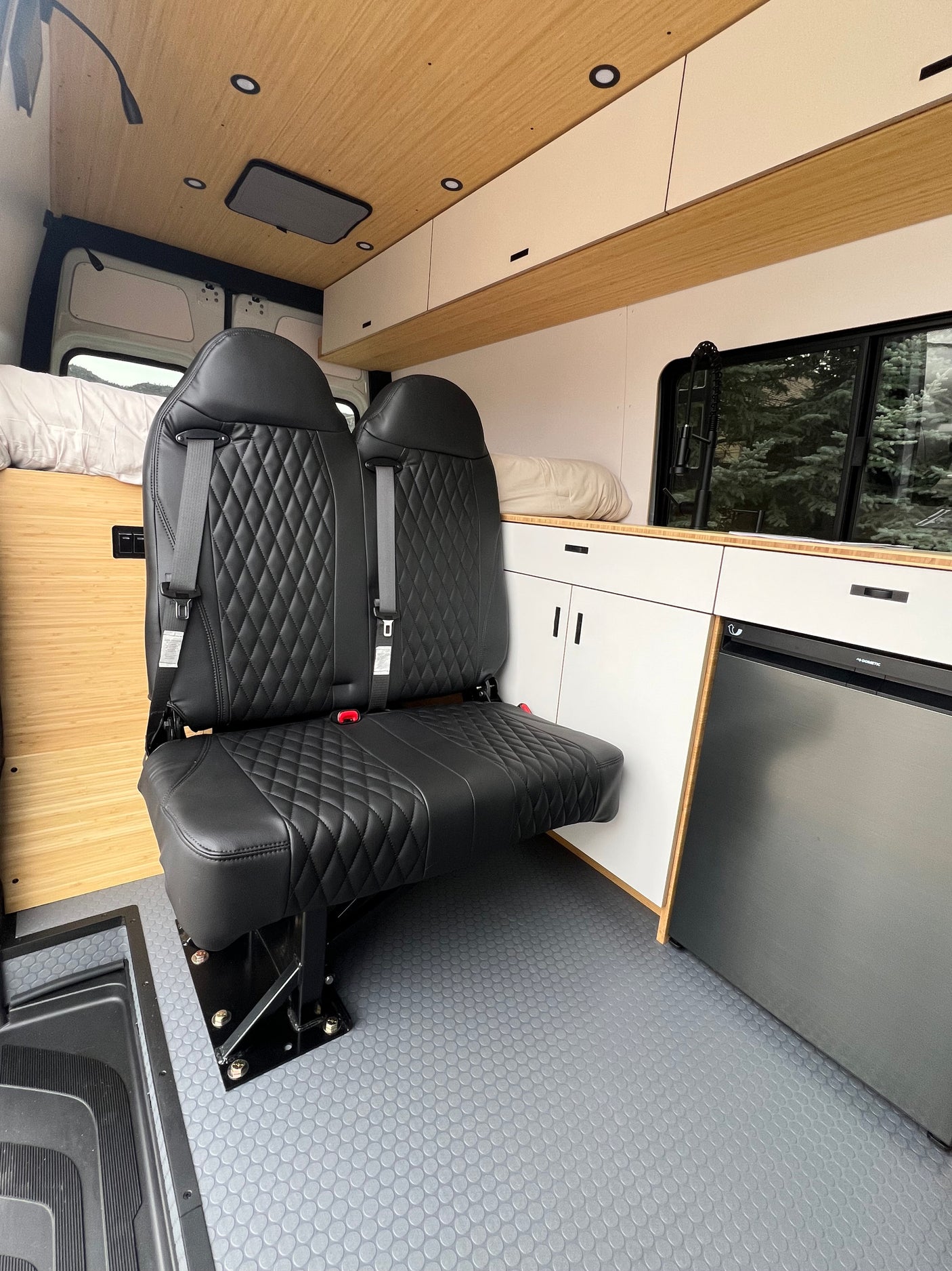 RV rental interior: Two black quilted seats, bamboo ceiling, white cabinets, and a fridge on gray flooring. Ready for travel!