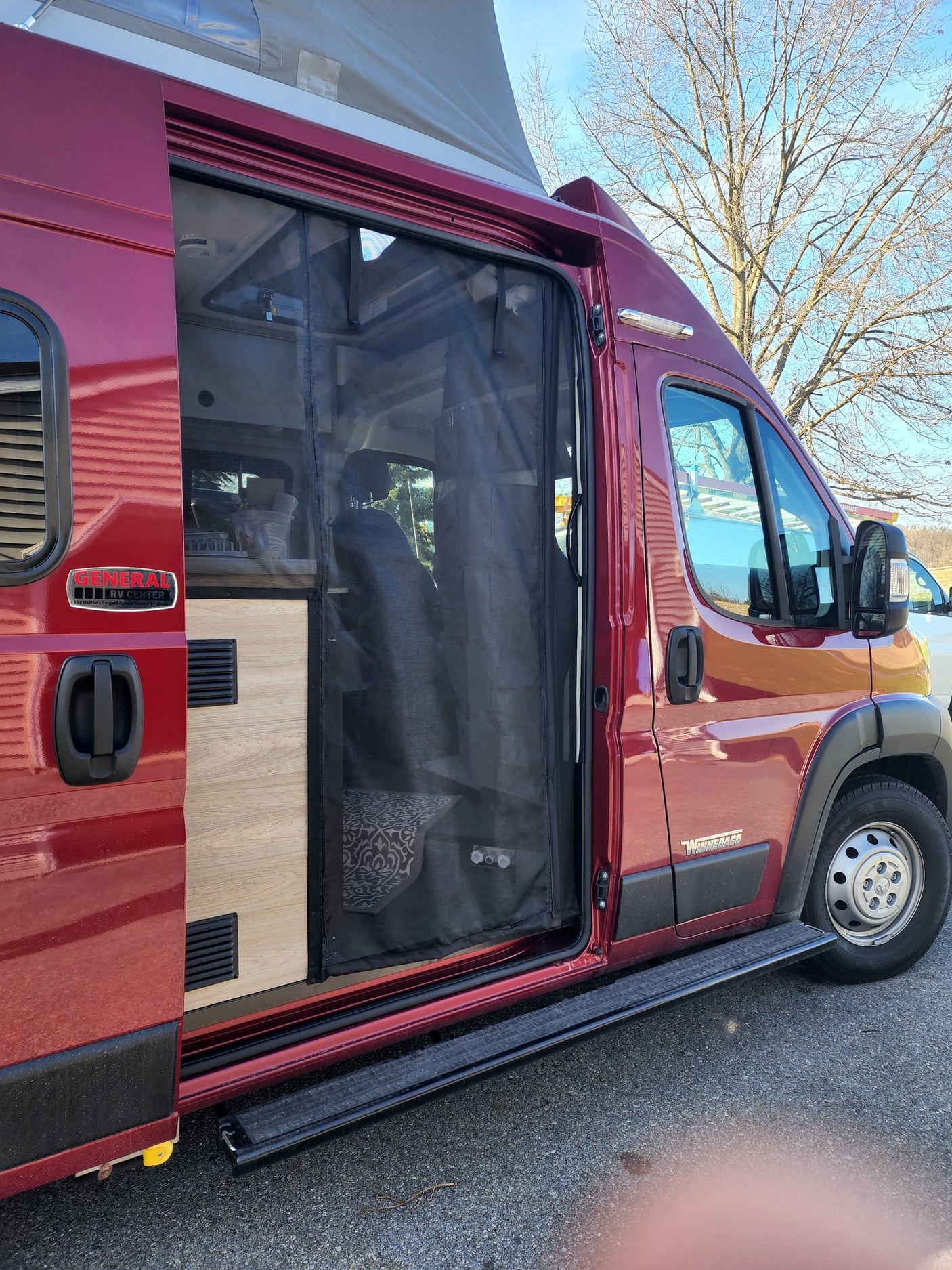 Maroon Winnebago camper van with open side door revealing mesh screen and interior, ideal for rv rental.