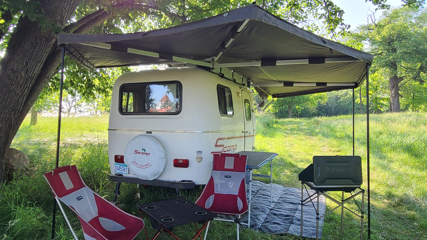 **RV rental** setup with an extended awning, chairs, and tables, perfect for outdoor camping in a grassy field.