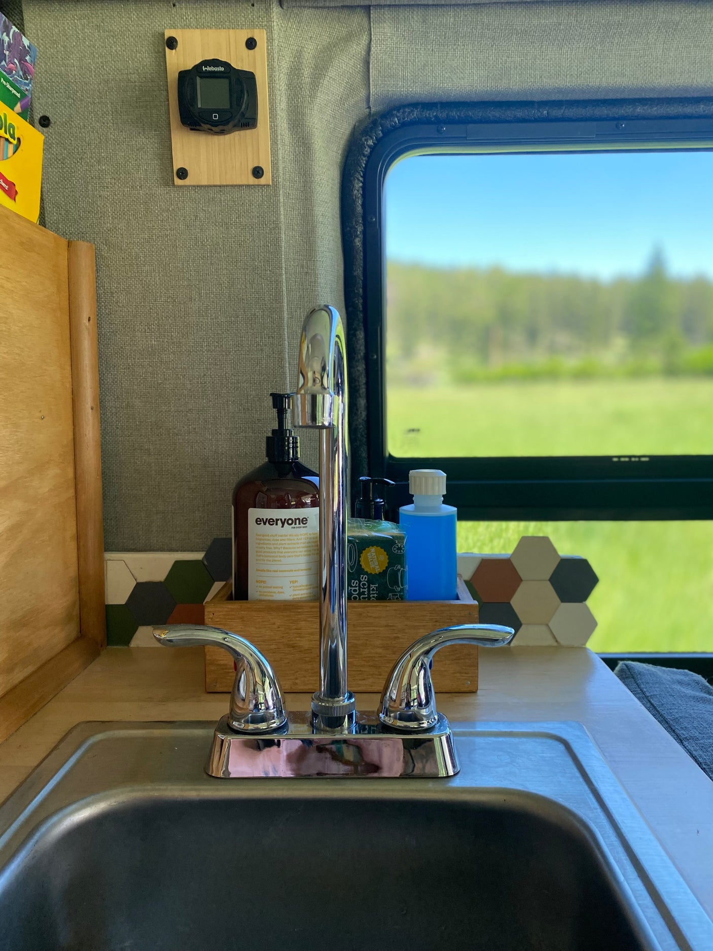 The sink area in an RV rental, featuring a chrome faucet, soap, Webasto control, and a serene window view.