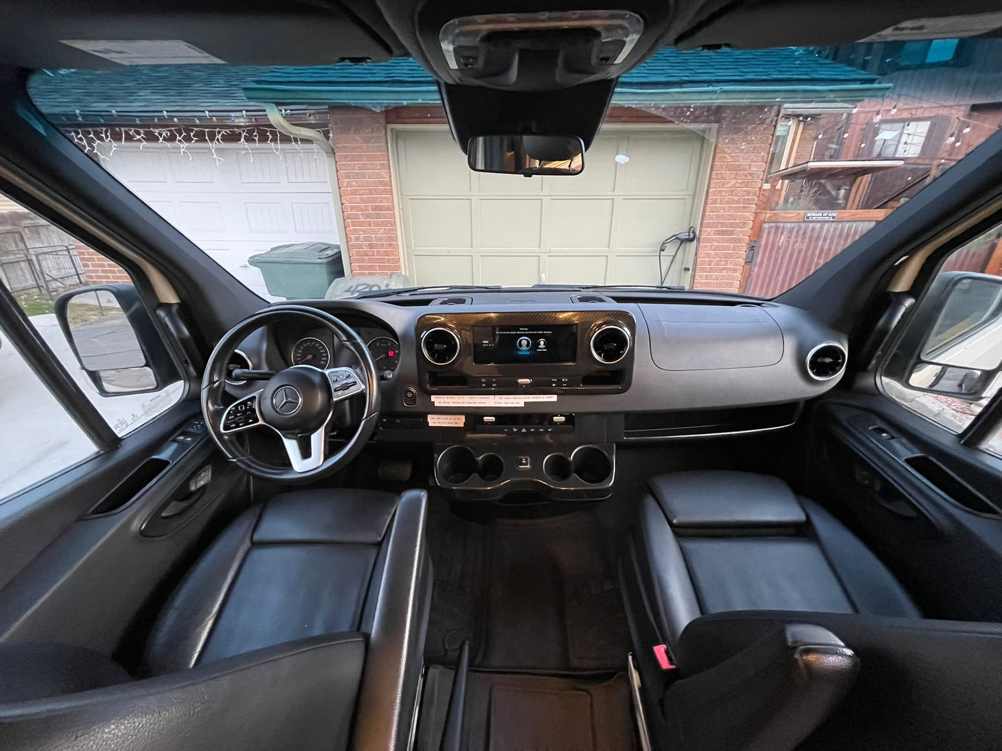 RV rental interior view: Dashboard, steering wheel, and front seats, with a house visible through the windshield.