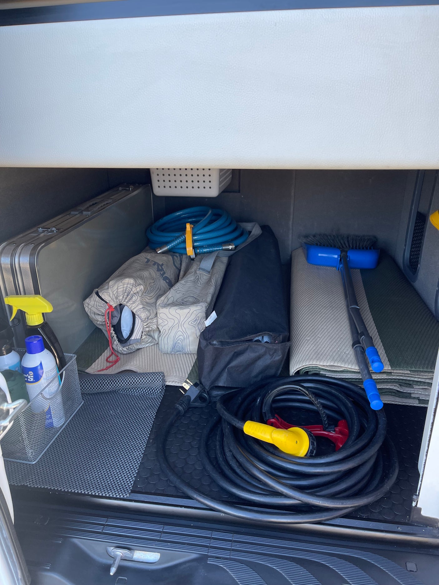 RV rental storage: neatly organized camping gear including power cord, water hose, table, broom, and cleaning supplies.