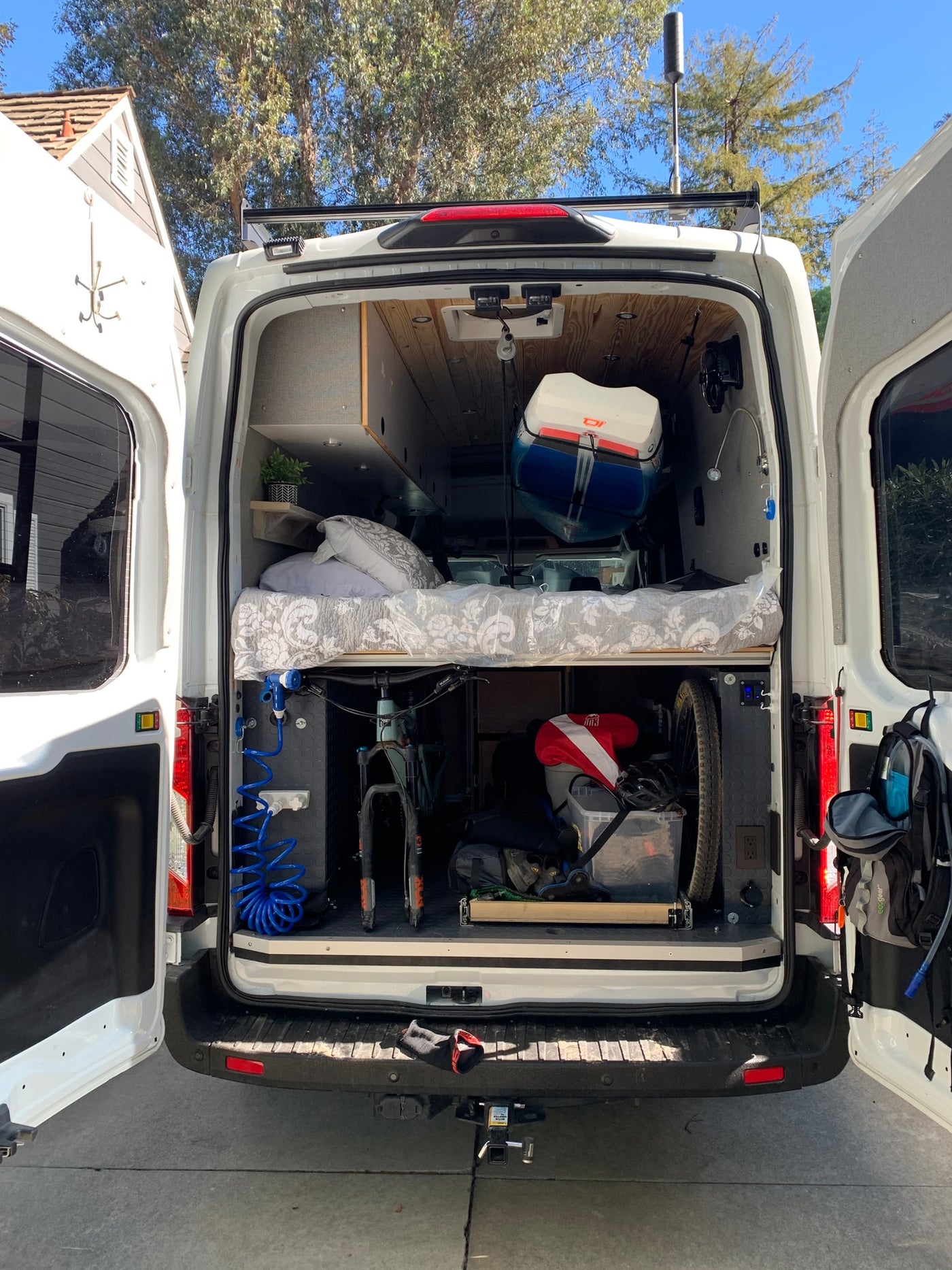 This RV rental campervan's rear reveals a cozy bed, bike storage, kayak, and gear for adventure-ready road trips. — photo 2