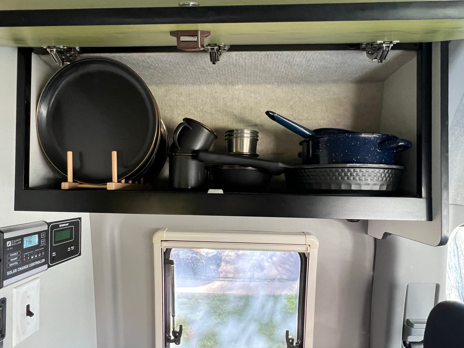 RV rental: An organized kitchen cabinet with black plates, pots, and pans, plus a Zamp Solar charge controller display.