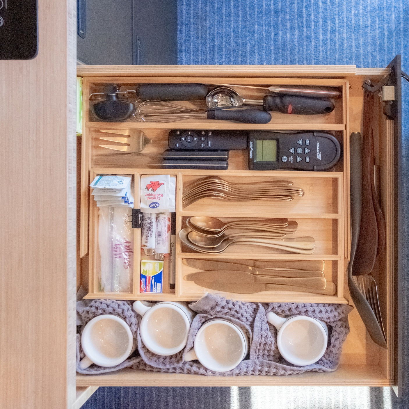 Compact rv rental kitchen drawer: organized cooking utensils, golden cutlery, and four nested cups.