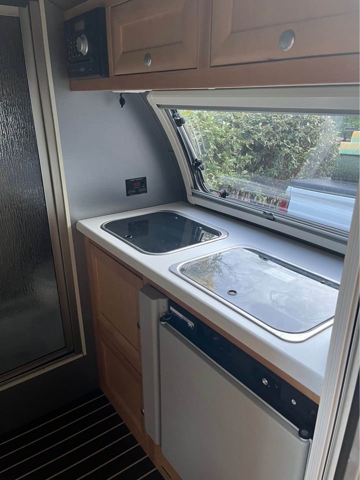 perfect for a nature getaway.|RV rental offers a peaceful lakeside camping view. Open window reveals a gravel site & BBQ grill.|Compact RV rental kitchen with sink