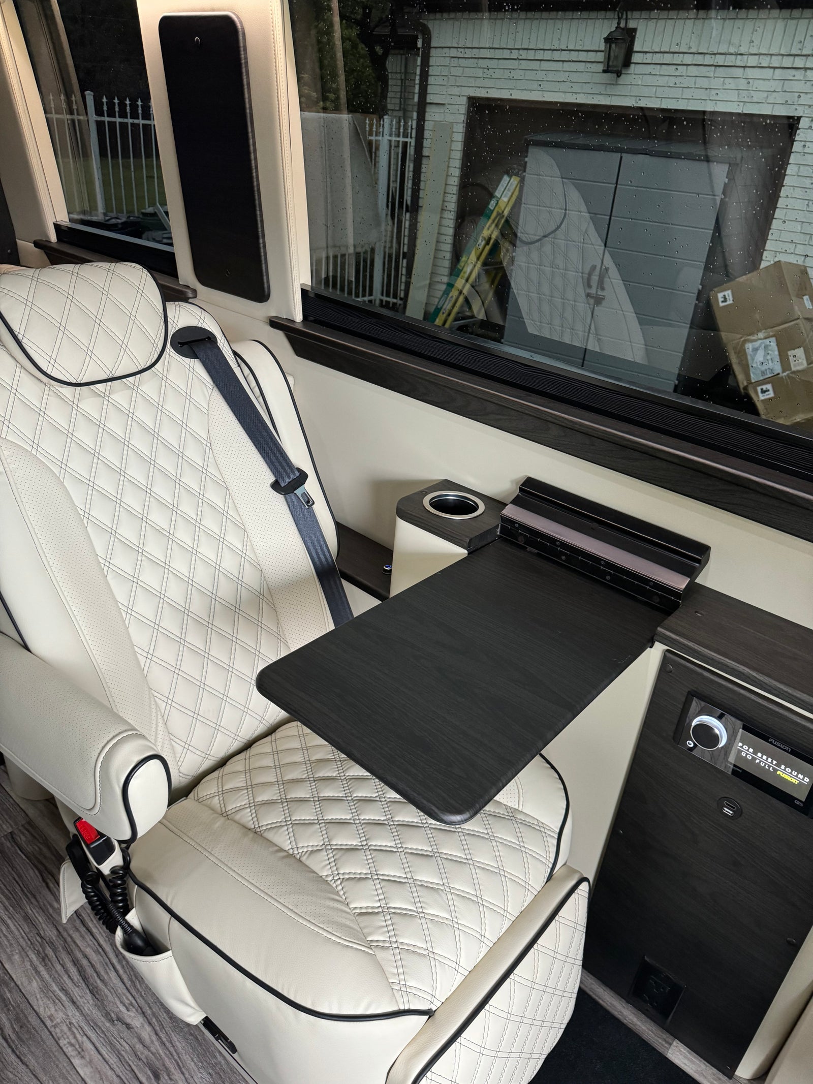 Enjoy luxury travel in this RV rental with a comfortable white leather seat, fold-out table, and integrated entertainment system.