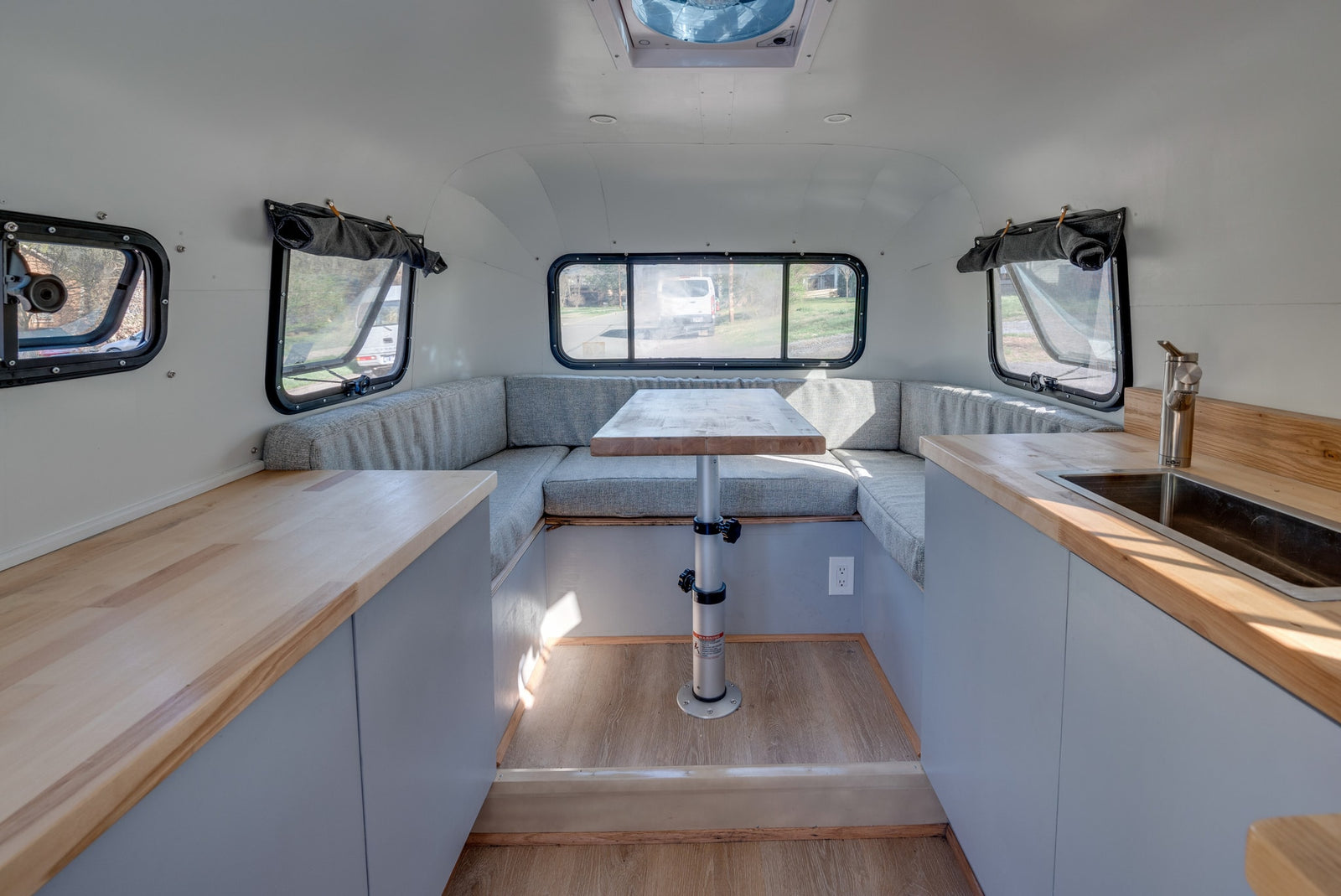 Bright rv rental interior: U-shaped dinette with table, light wood kitchenette counters, and rear windows for views.