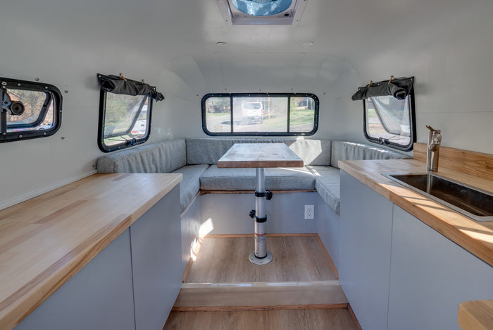 Bright rv rental interior: U-shaped dinette with table, light wood kitchenette counters, and rear windows for views.