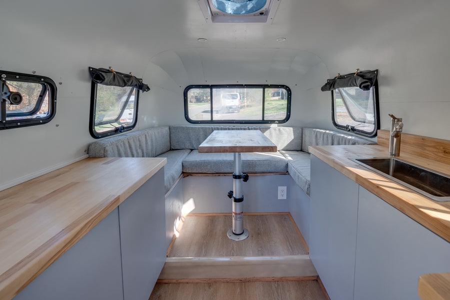 Bright rv rental interior: U-shaped dinette with table, light wood kitchenette counters, and rear windows for views.