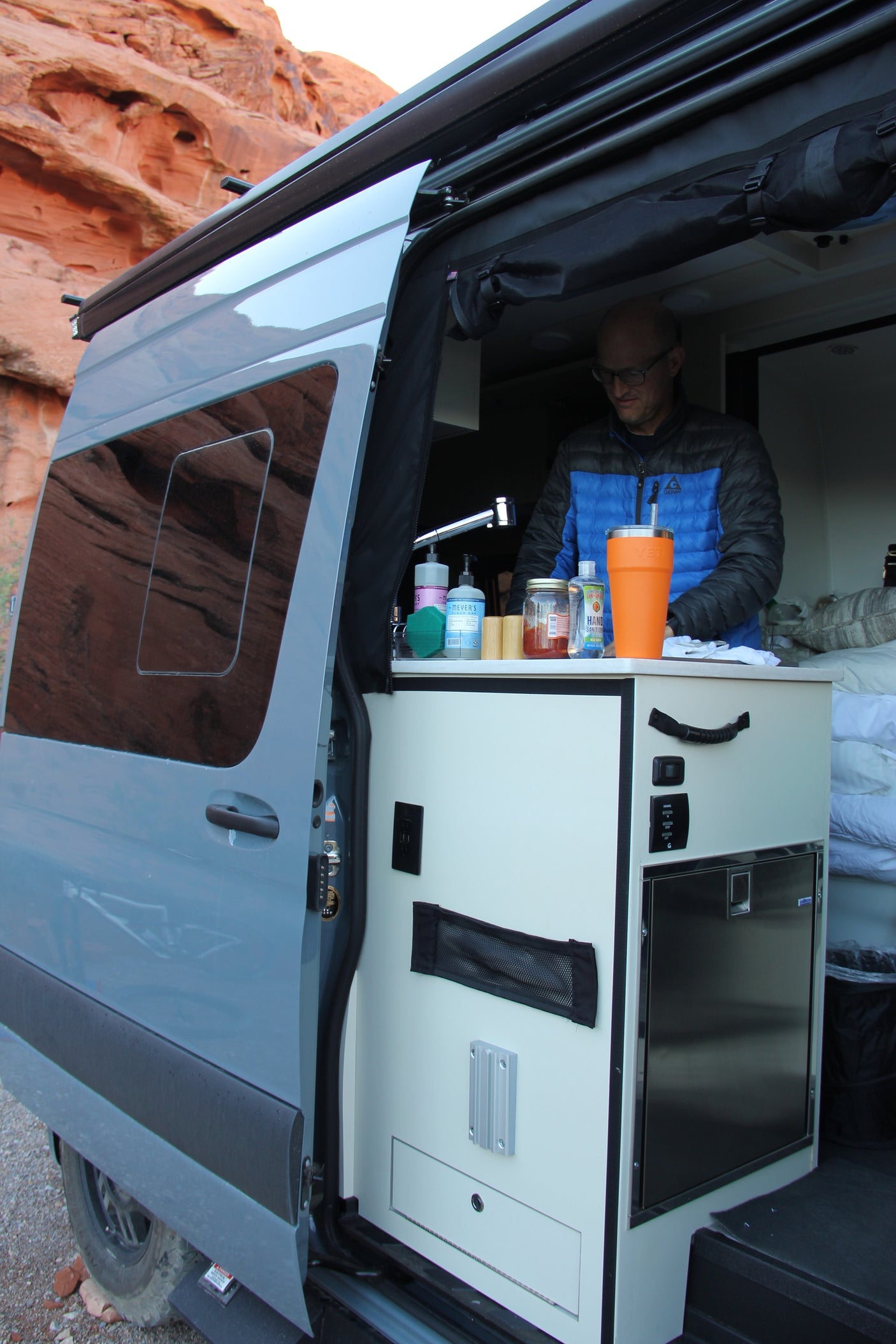 Man inside a grey **rv rental** van with an open side door, showcasing the built-in kitchen and countertop.