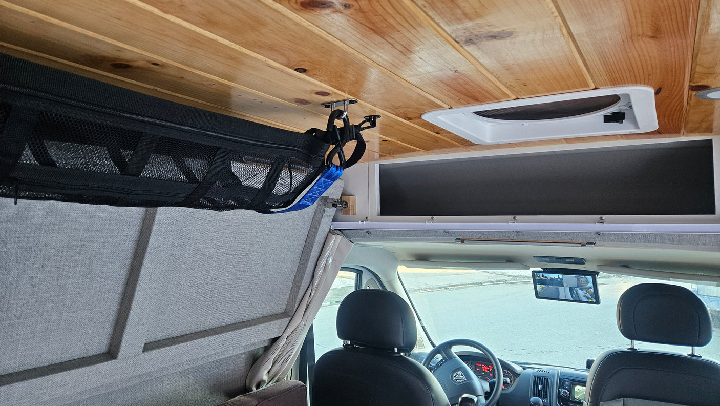 Interior of an RV rental: wooden ceiling, front cab with multi-view rearview screen, and mesh overhead storage.
